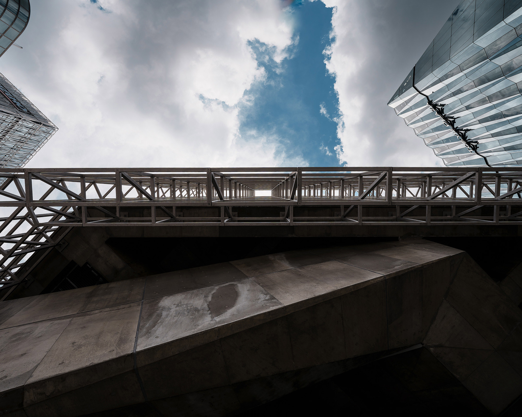外観。地上から仰ぎみたグリッド状のファサード越しに雲がかかった空が広がる。