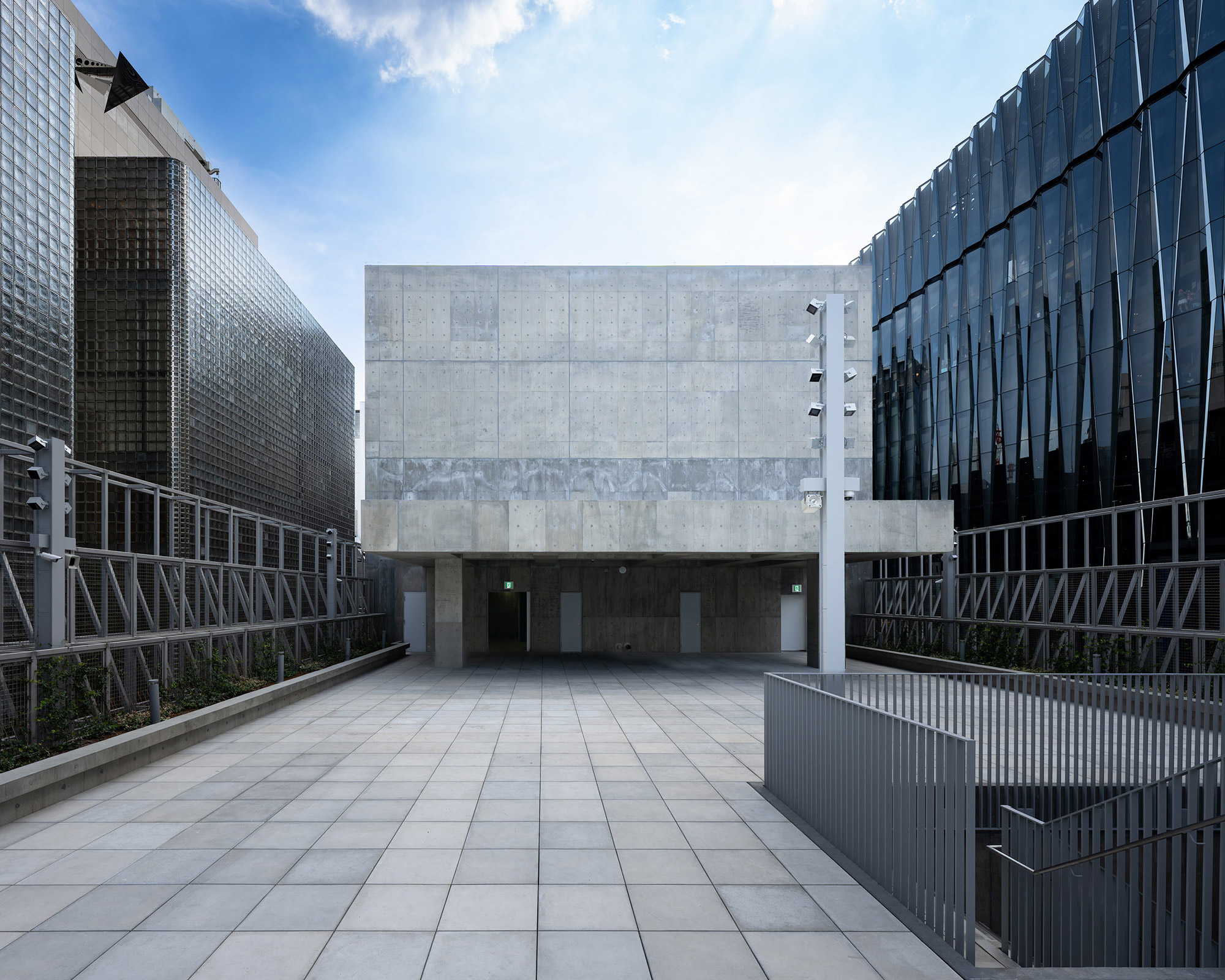 外観。周囲の建物よりも低く構えた屋上階で、青空のもとコンクリートの塔屋と東屋がある。