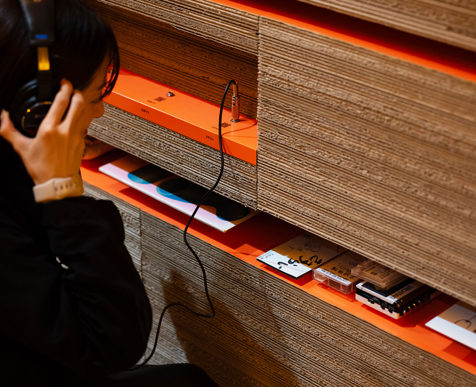 展示風景。ヘッドフォンをつけた人が、地層のような壁面に設置されたオーディオジャックを使って音楽を聴いている。
