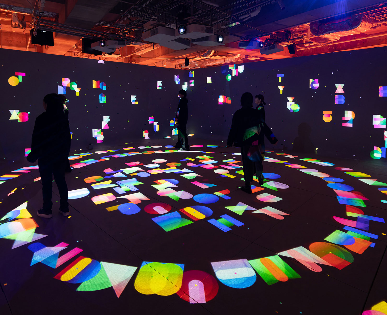 展示風景。暗い空間の中にさまざまなオブジェクトがプロジェクションされ、その様子を数人の人が眺めている。
