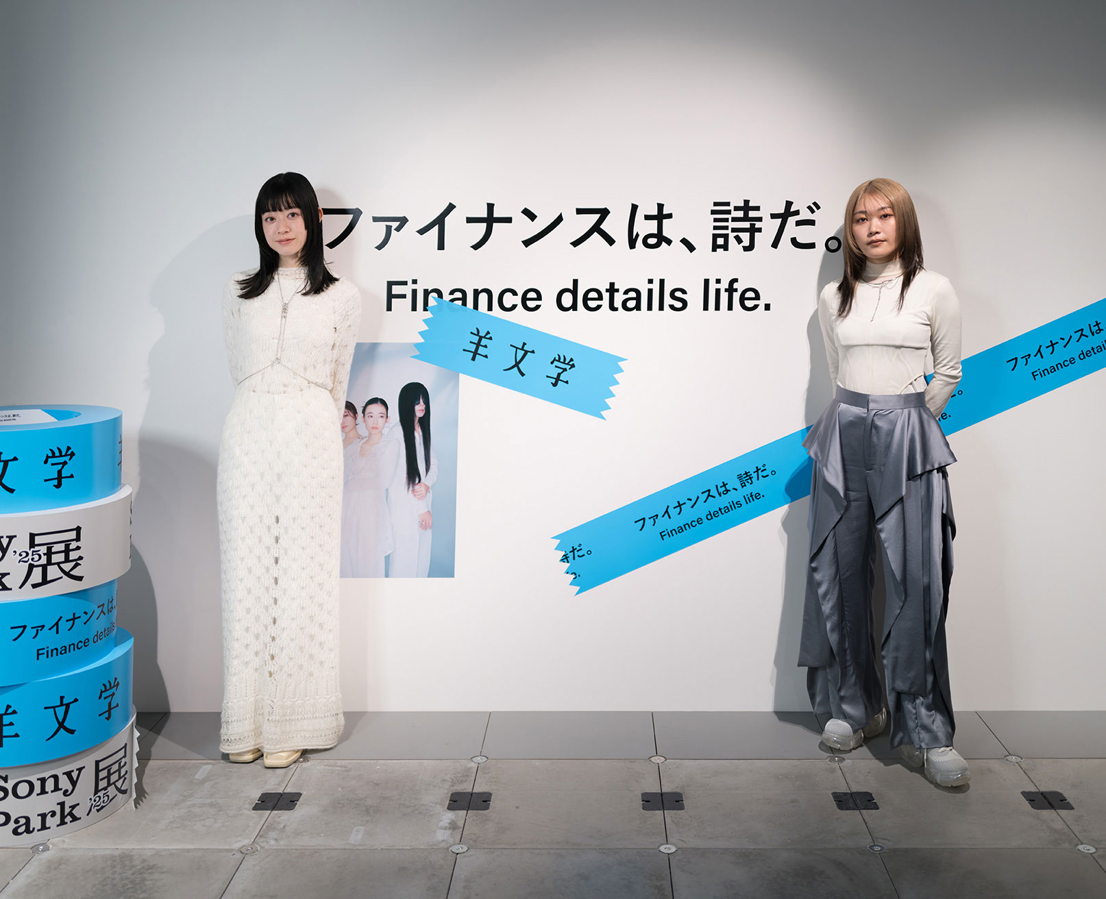 「ファイナンスは、詩だ」というメッセージが書かれた展示壁の前に立つ2人の女性。