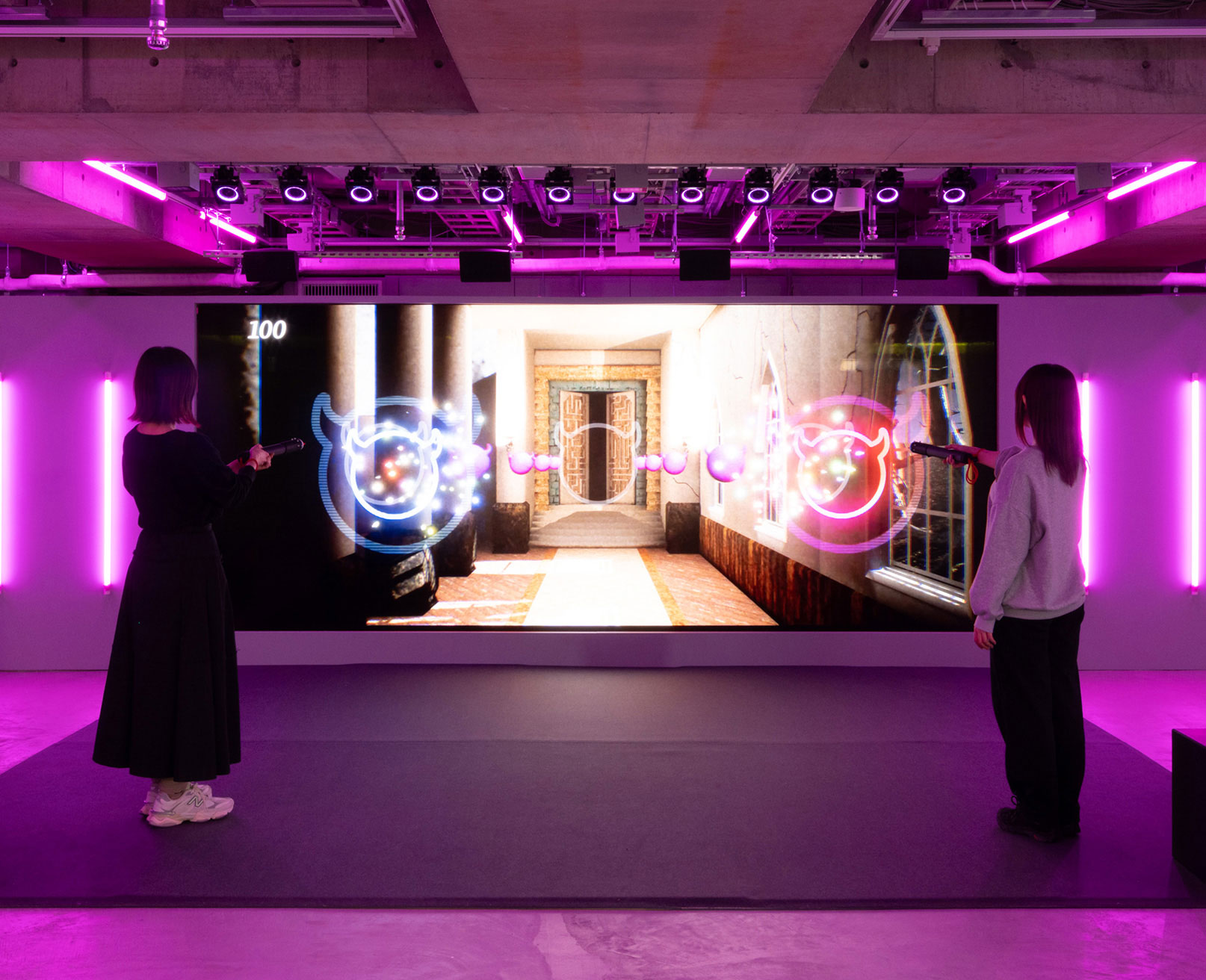 展示風景。スクリーンの前に立つ2人の来場者が、デジタルシューティングゲームをプレイしている様子。