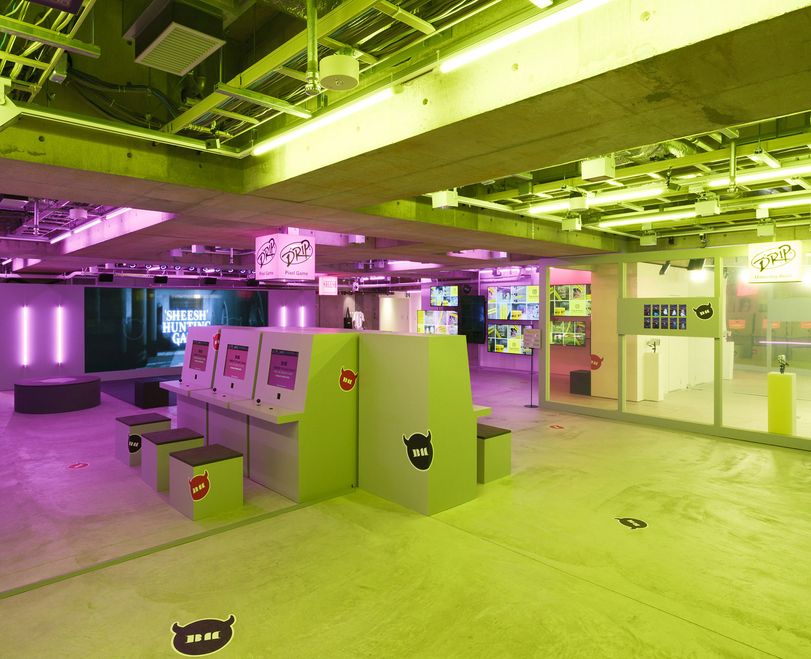 展示風景。ピンクと黄色の照明が印象的な空間に、ゲームのスクリーンとプレイ用の端末が設置されている。