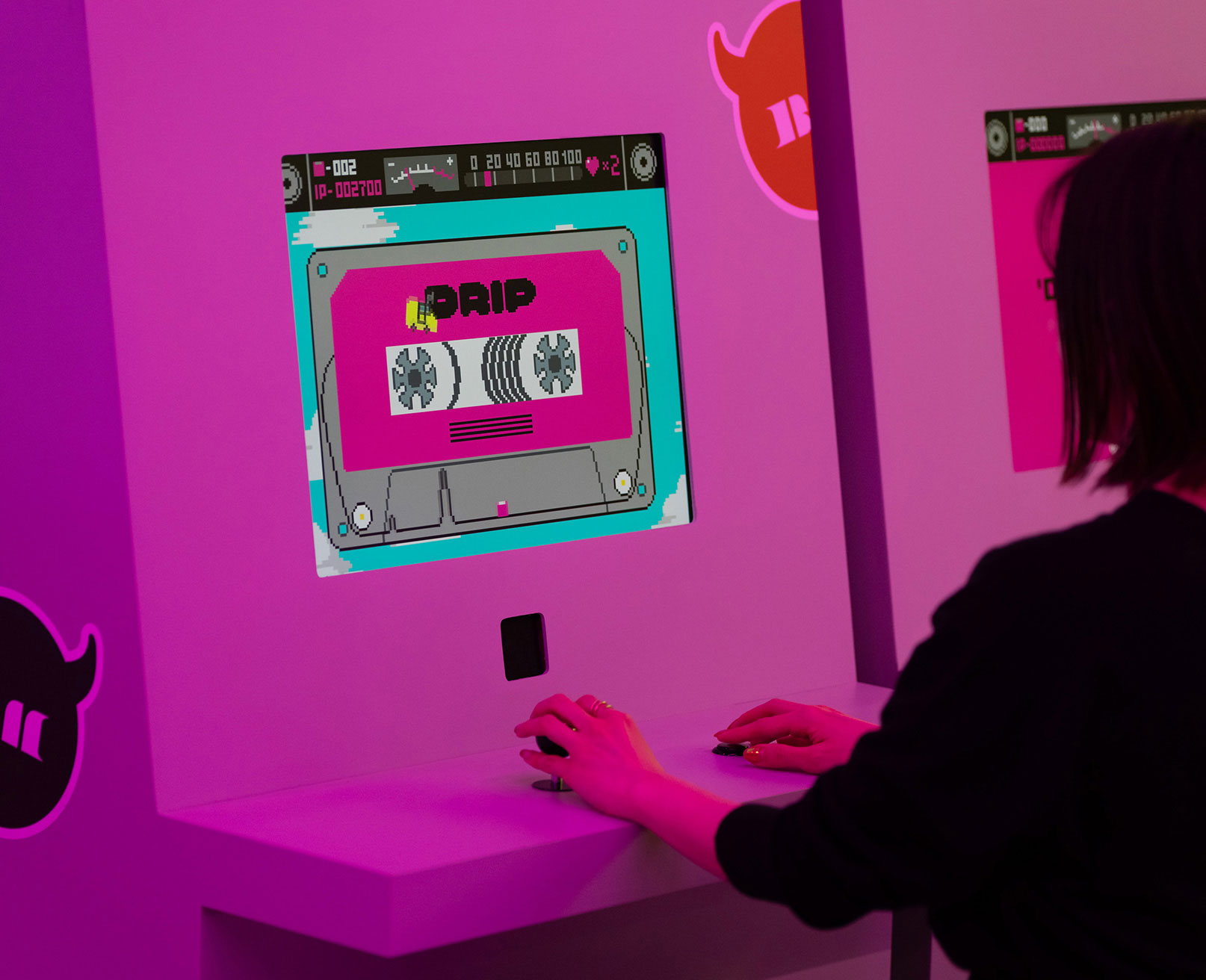 展示風景。ゲーム端末のスクリーンにカセットテープ風のグラフィックが表示され、来場者が操作している。