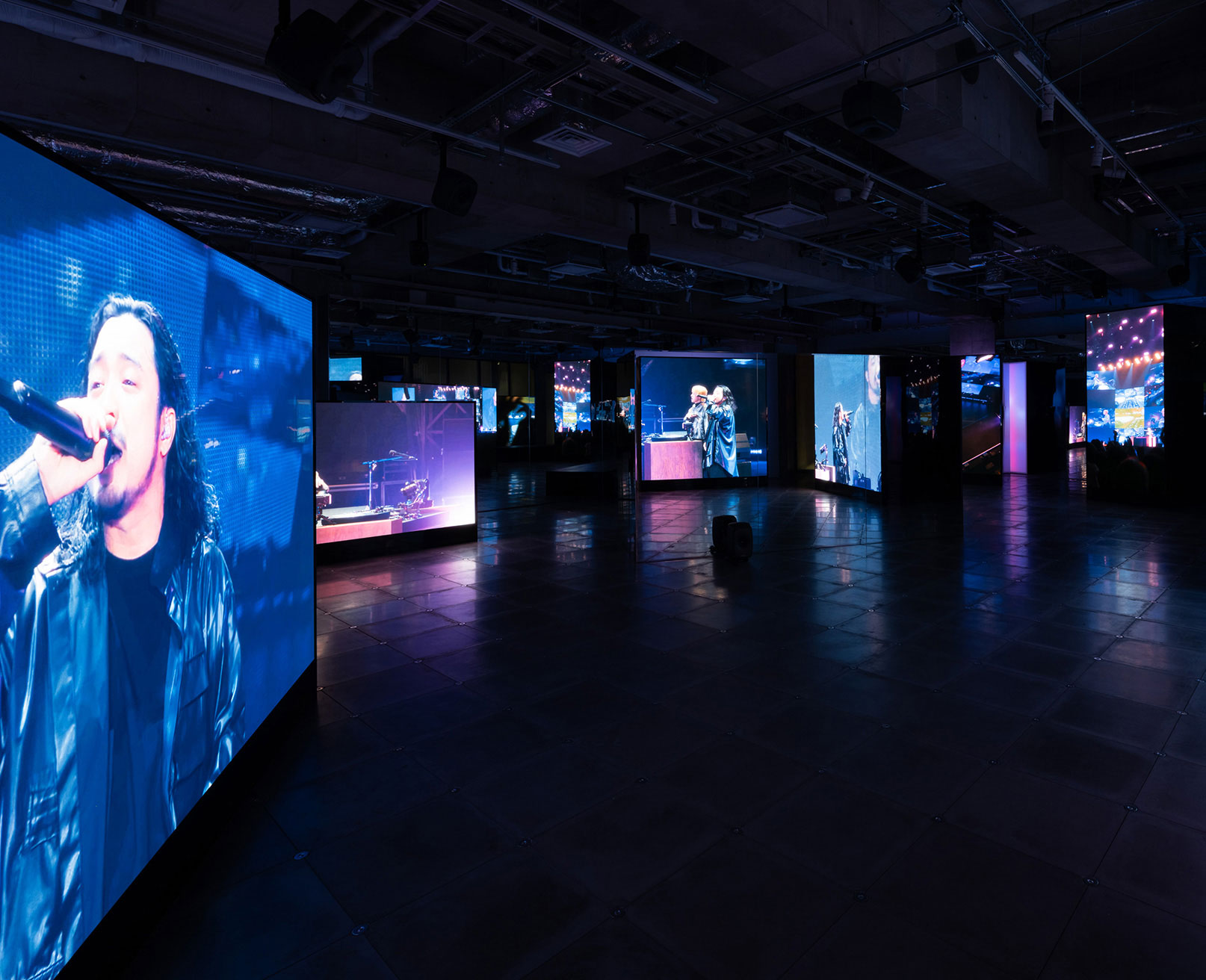 展示風景。薄暗い空間の中で、ライブパフォーマンスの様子が映し出された大型スクリーンが設置されている。