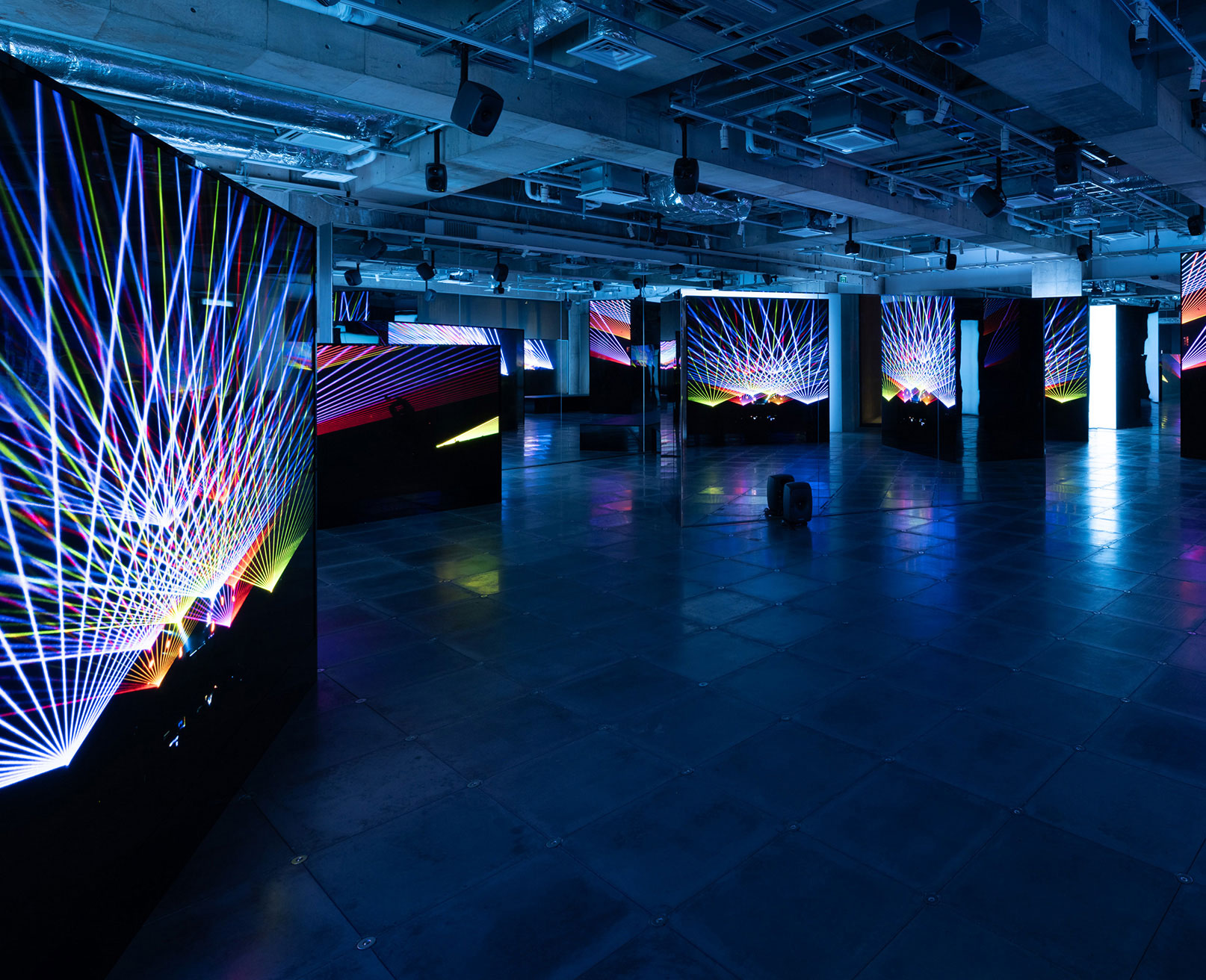 展示風景。薄暗い空間の中で、鮮やかなレーザーグラフィックが映し出されたスクリーンが設置されている。