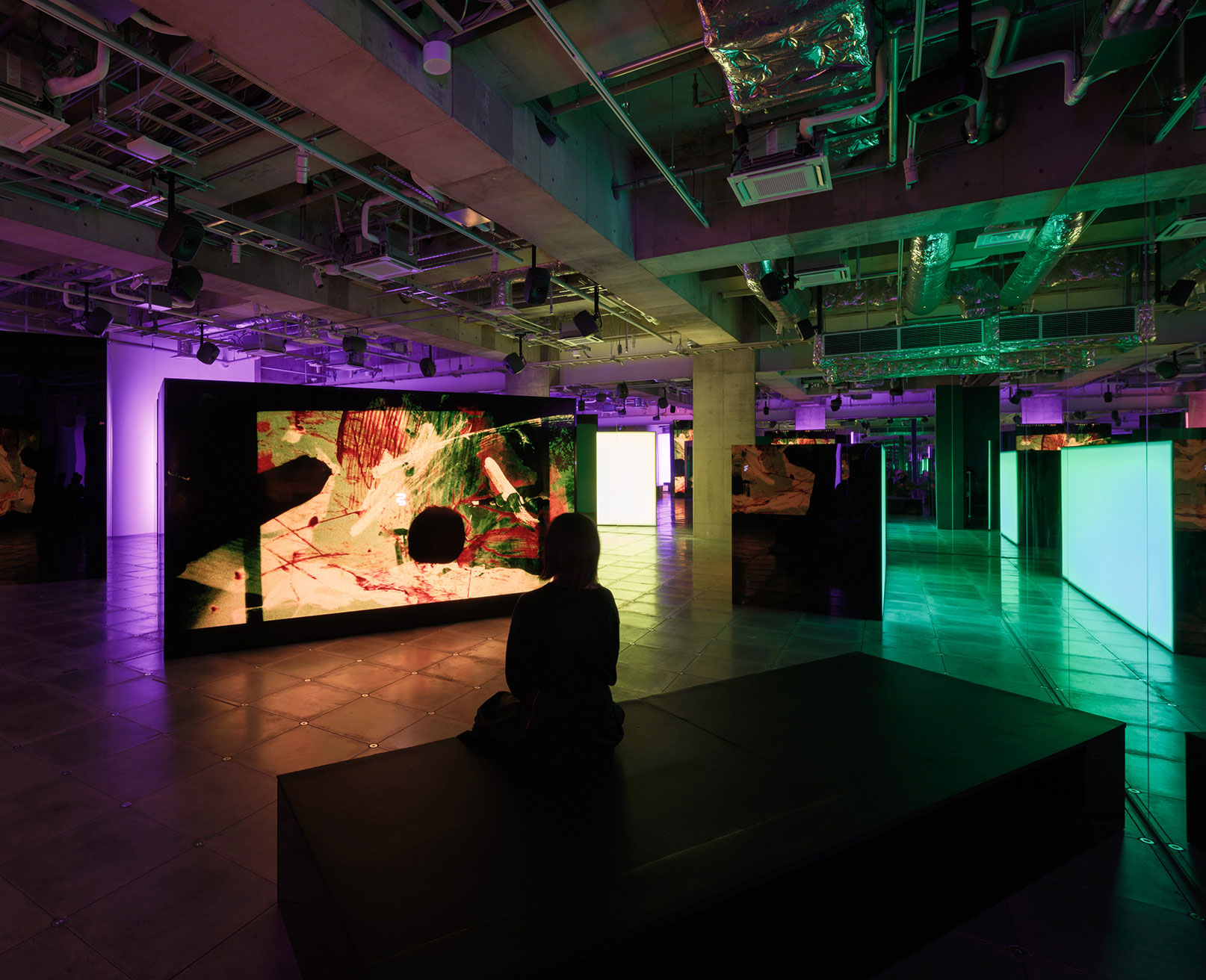 展示風景。色彩豊かなアニメーションが映し出されたスクリーンの前に、ベンチに座って鑑賞する来場者がいる。