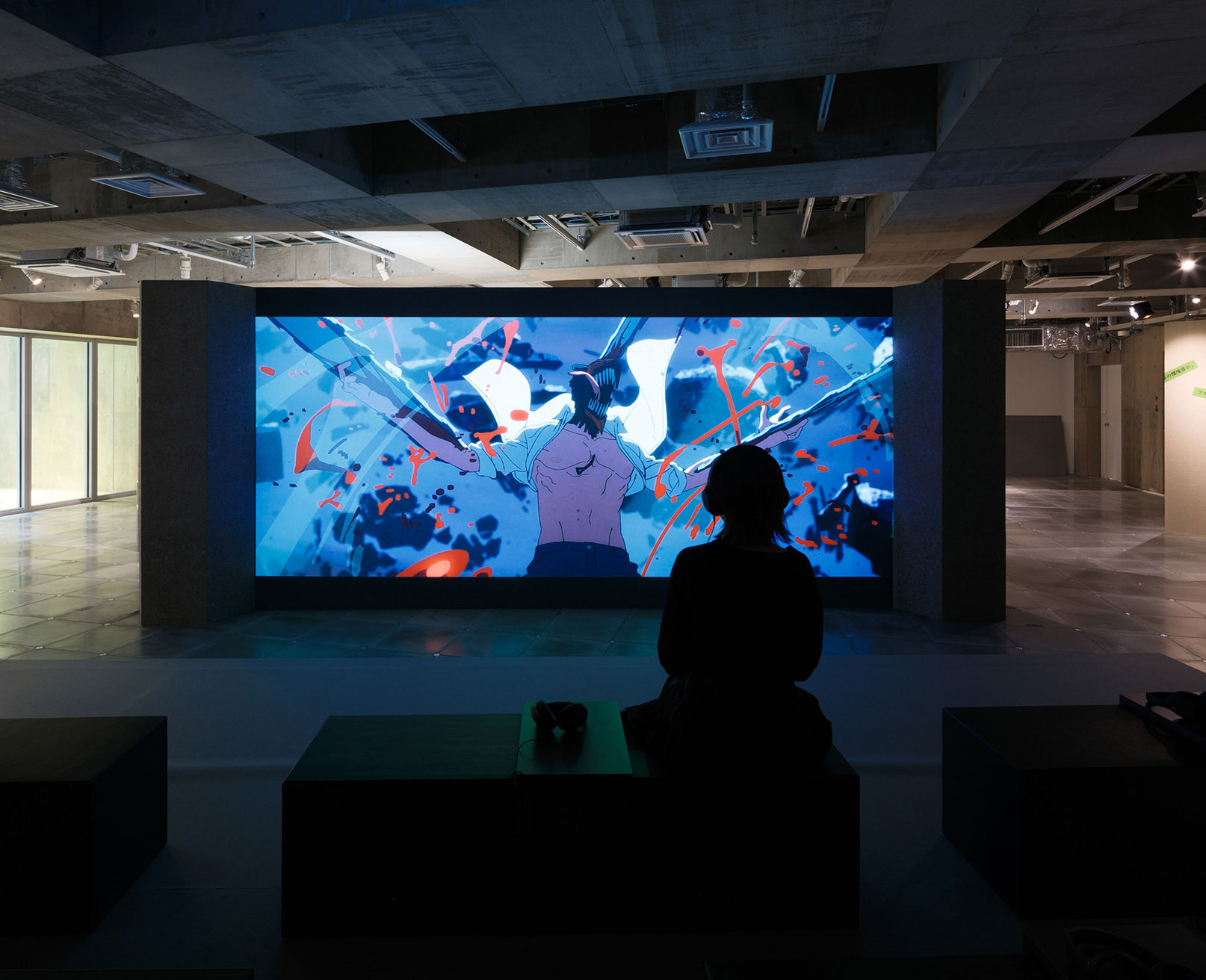 展示風景。スクリーンに映し出されたアニメーション映像を、来場者がベンチに座って鑑賞している。