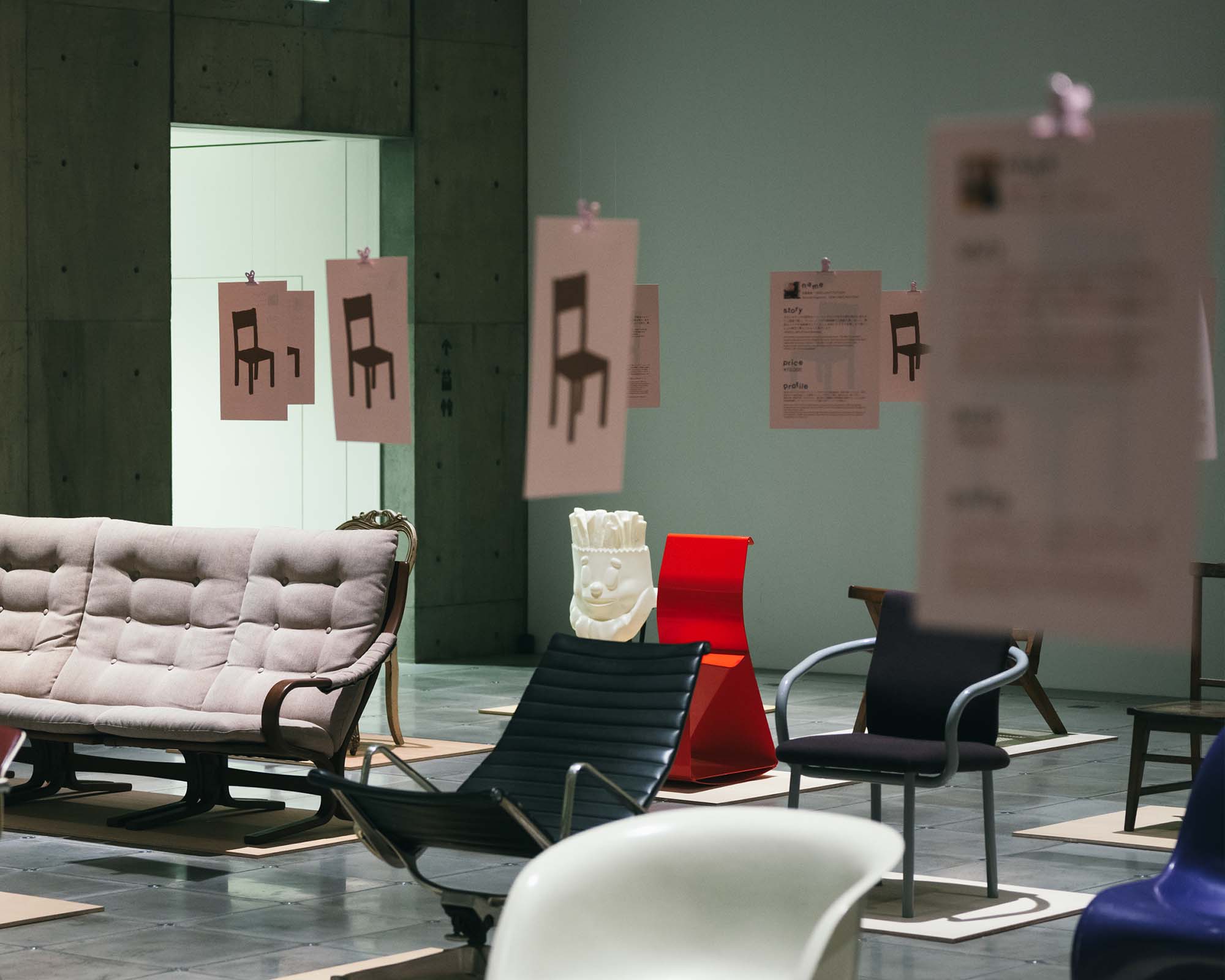 Ginza Sony Parkの展示空間に、多様な椅子が等間隔に配置される。吊るされた図版が揺れ、デザインの背景を静かに伝える構成。