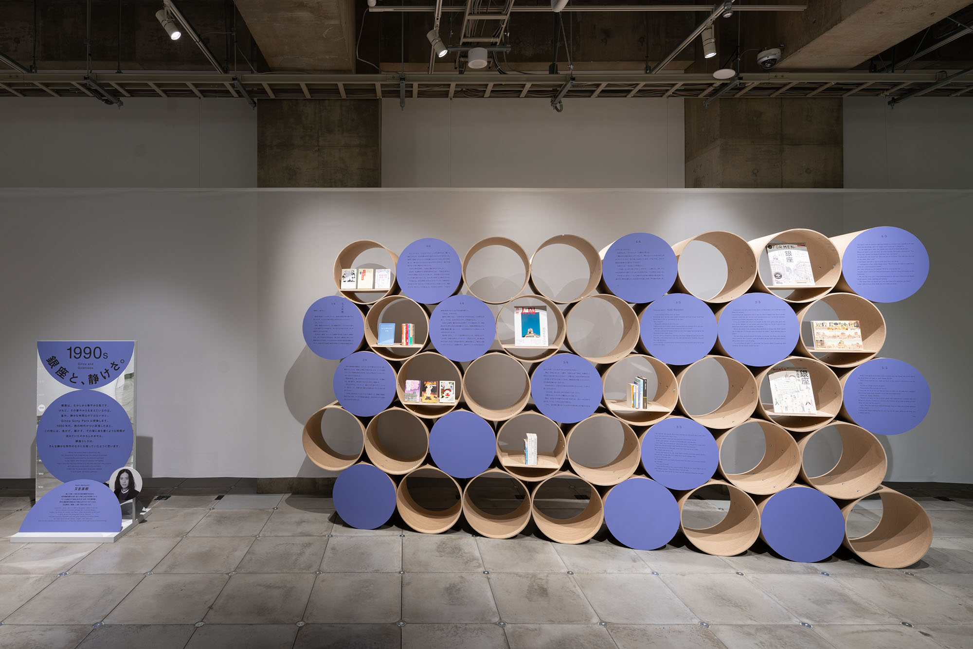 1990s section “Ginza and Quietness.” Cylindrical shelves and panels display essay texts about Ginza written by Naoki Matayoshi.