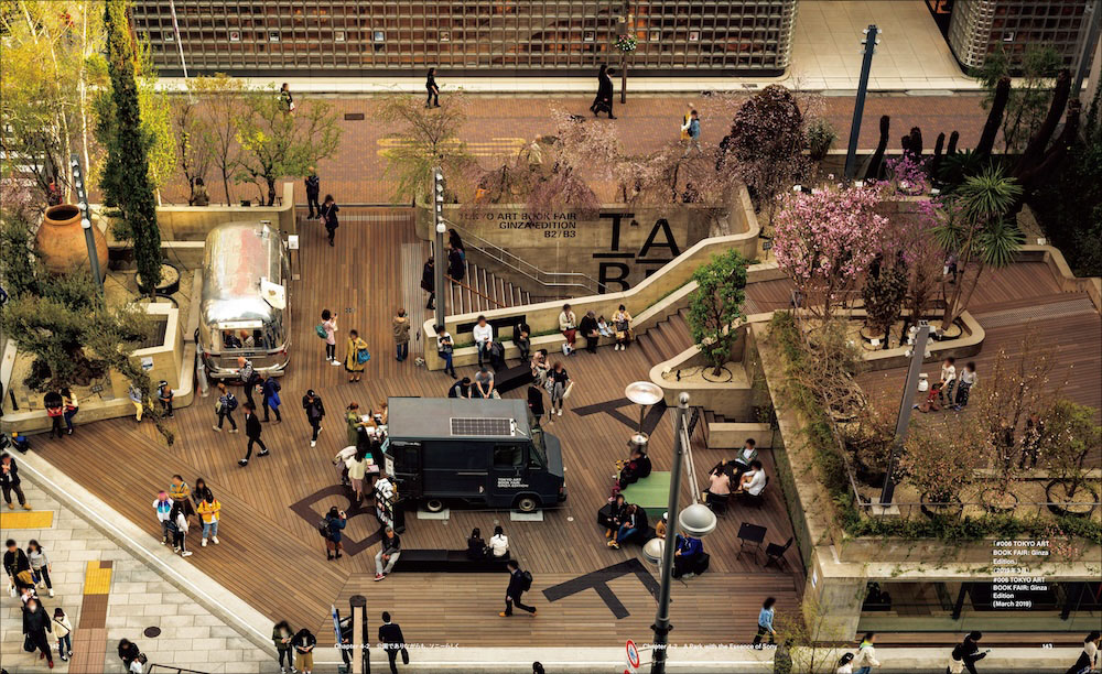 書籍の見開きページ。Ginza Sony Park バージョンフラットの時代の地上階を上空から見下ろした写真。ウッドデッキの広場にキッチンカーが停まり、多くの人々がベンチに座ったり歩いたりしている。