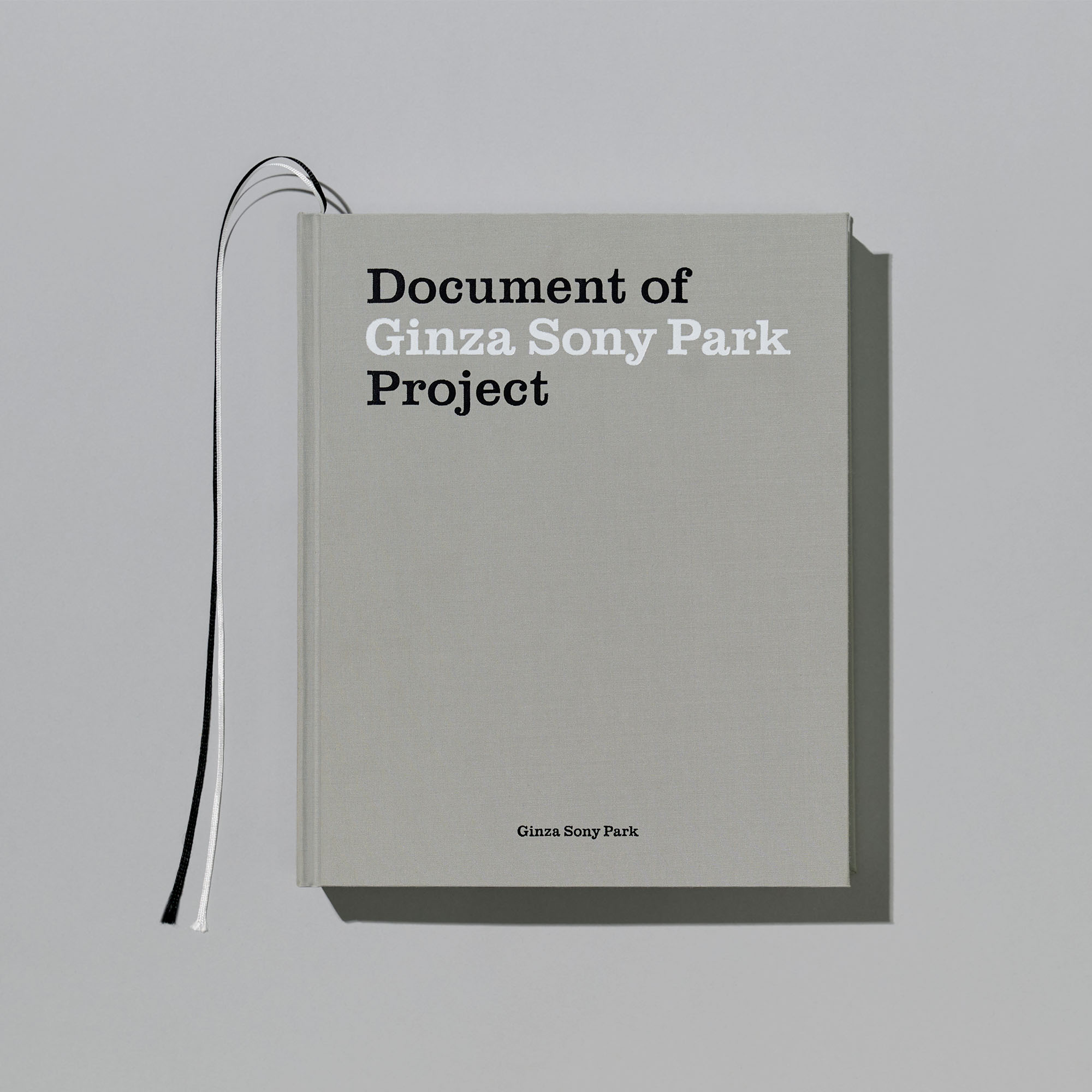 グレーのシンプルな表紙の書籍。中央上部に黒と白の文字で「Document of Ginza Sony Park Project」とタイトルが印刷されており、左側から白と黒の2本のしおり紐が出ている。