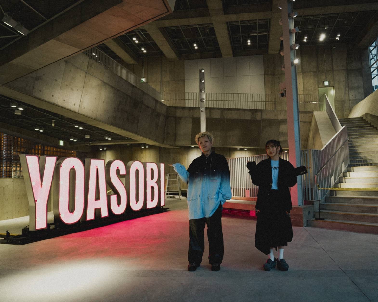 内観。YOASOBIのネオンサインの前でポーズを取るYOASOBIの二人。