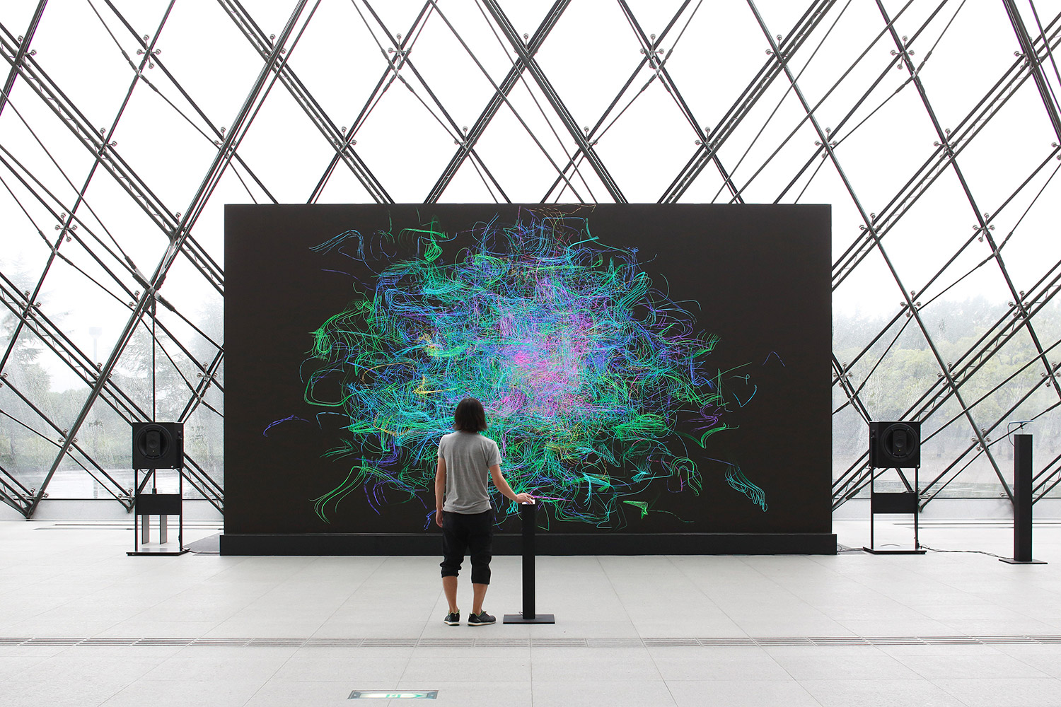 Sensing Streamsの展示イメージ画像。大きなモニターに立っている男性が、右手をコントローラの上に置いている。