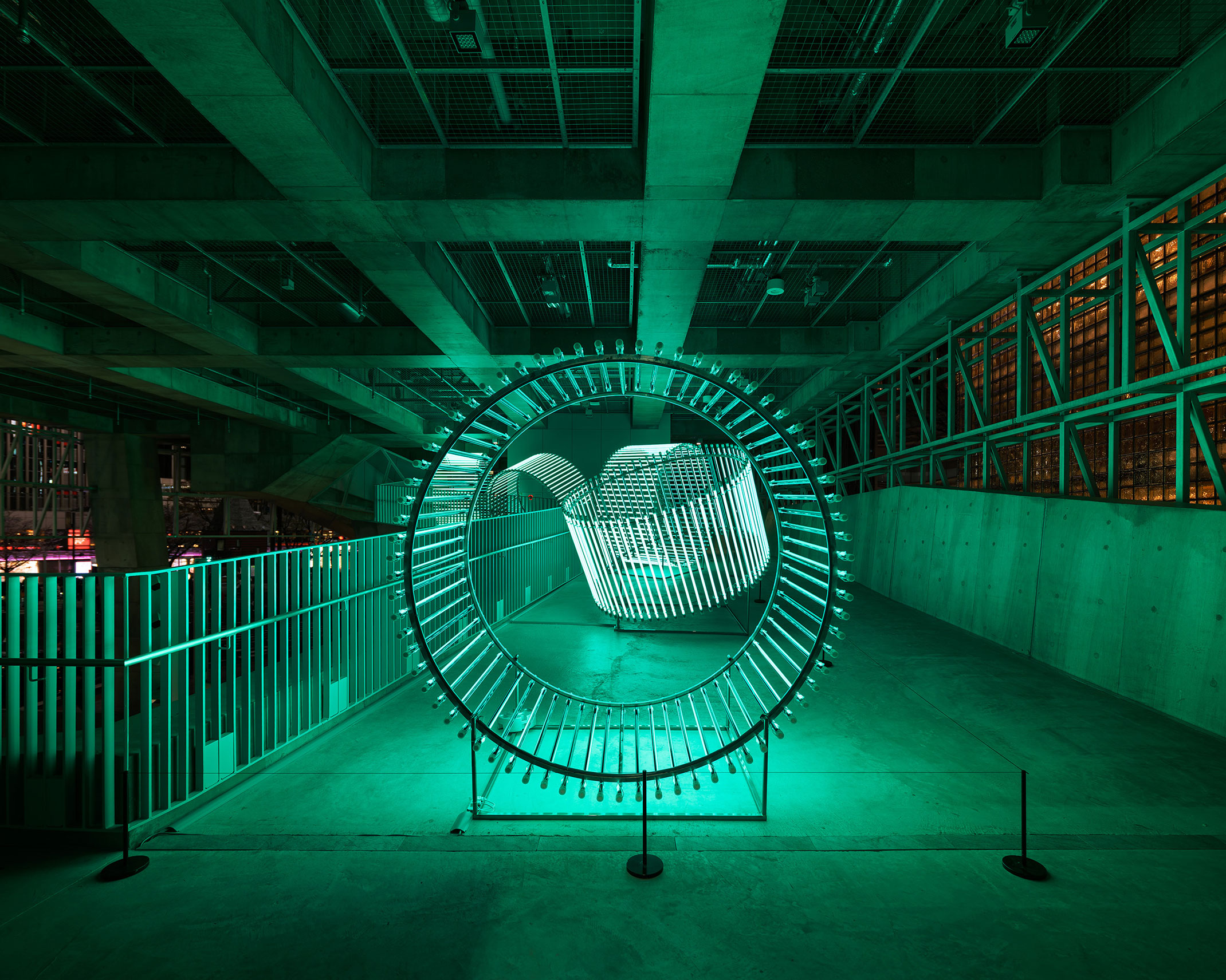 展示風景。コンクリート建築の空間で緑色の円環状のライトが光っている。