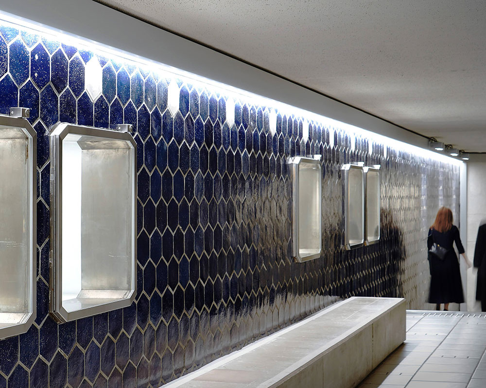 青いタイル壁のショーケースの奥に、階段を降りる男女いる。