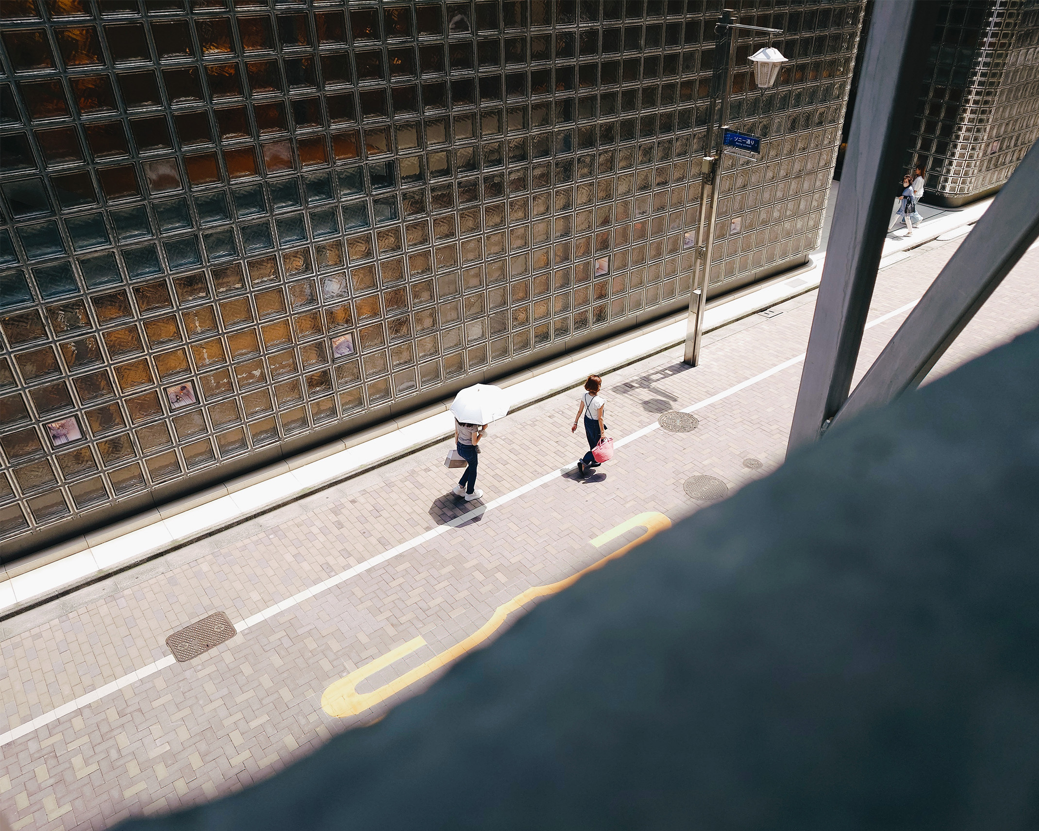 日傘をさした人とショッピングバッグを持った人が歩いている様子を、Ginza Sony Park内から見下ろした風景。