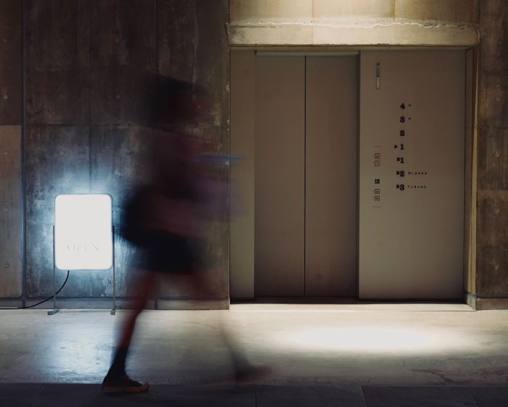 Ginza Sony Parkの夜の一角。コンクリート壁とエレベーター前を、通り過ぎる人影がぶれて写る。