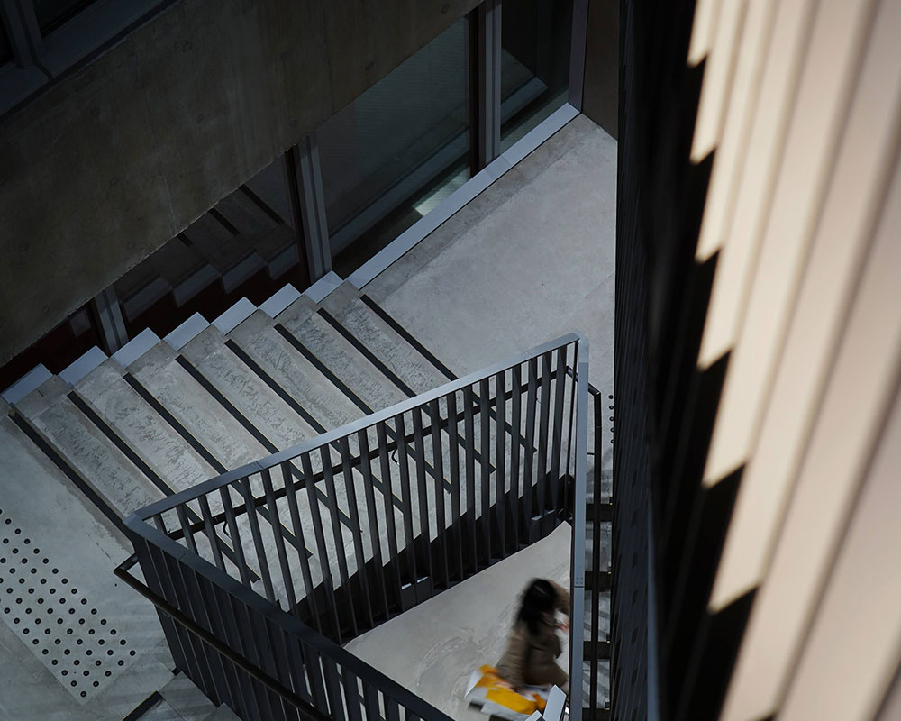 見下げた吹き抜け階段の先に人が歩いている。