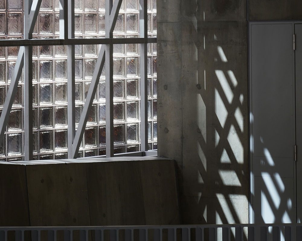 陽光が注ぎ、コンクリート建築の内壁にグリッド状のフレームの影が落ちている。