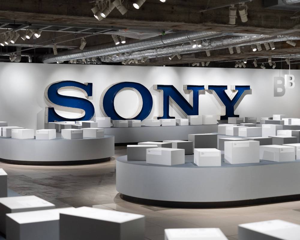 展示の様子。空港のバゲージクレームのような会場に、100個ほどの白い箱が集まっている。奥の壁面には「SONY」サインがある。