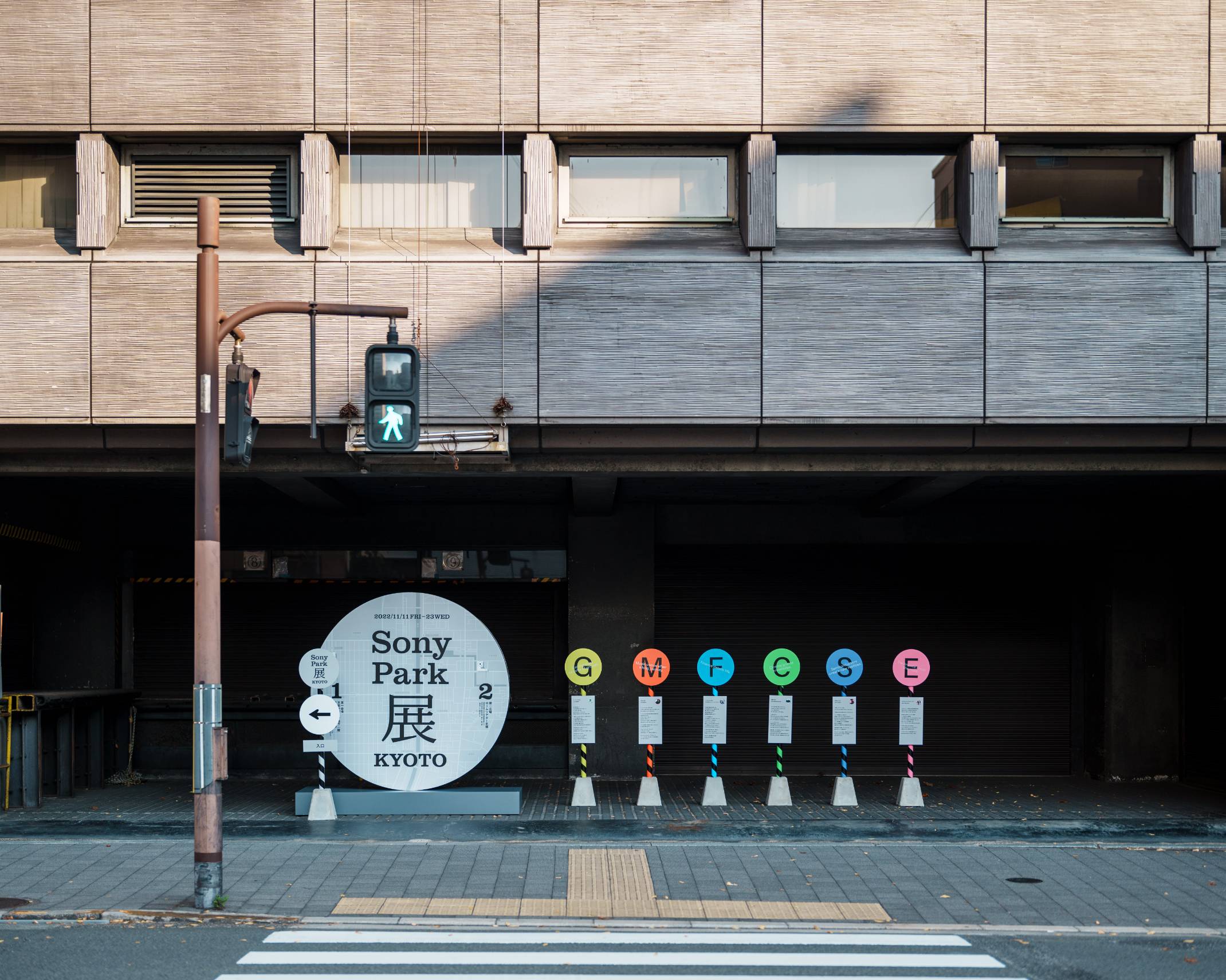 外観。屋外に、円形で表現されたメインビジュアルのサインと、6つのバス停のようなサインが並んでいる。