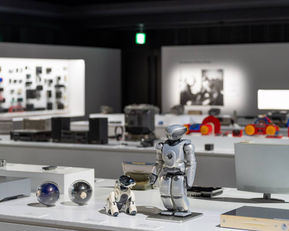 展示の様子。手前の展示台に、エンタテインメントロボット「aibo」、小型二足歩行エンターテインメントロボット「QRIO」や球体型の「Q.taro」が展示されている。