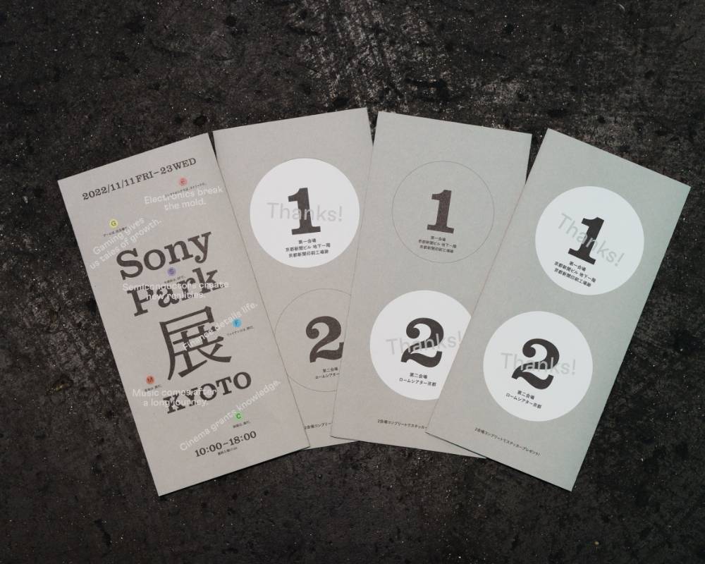 リーフレットの写真。表紙にはメインビジュアルがデザインされ、裏面には「1」「2」のステッカーが貼られている。