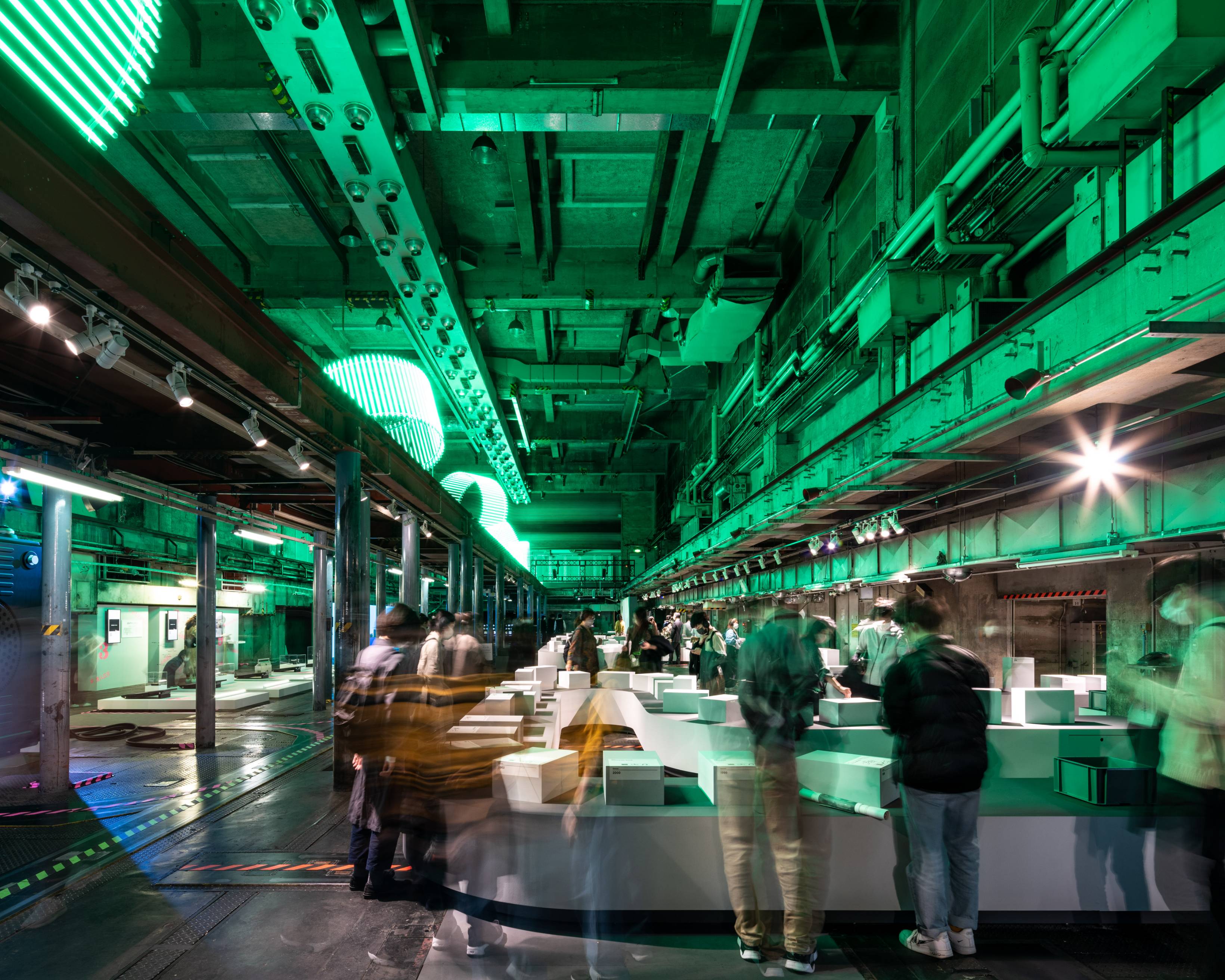 展示の様子。上層にある緑色に灯るオブジェの光が広がる地下空間の展示に人々が集まる。