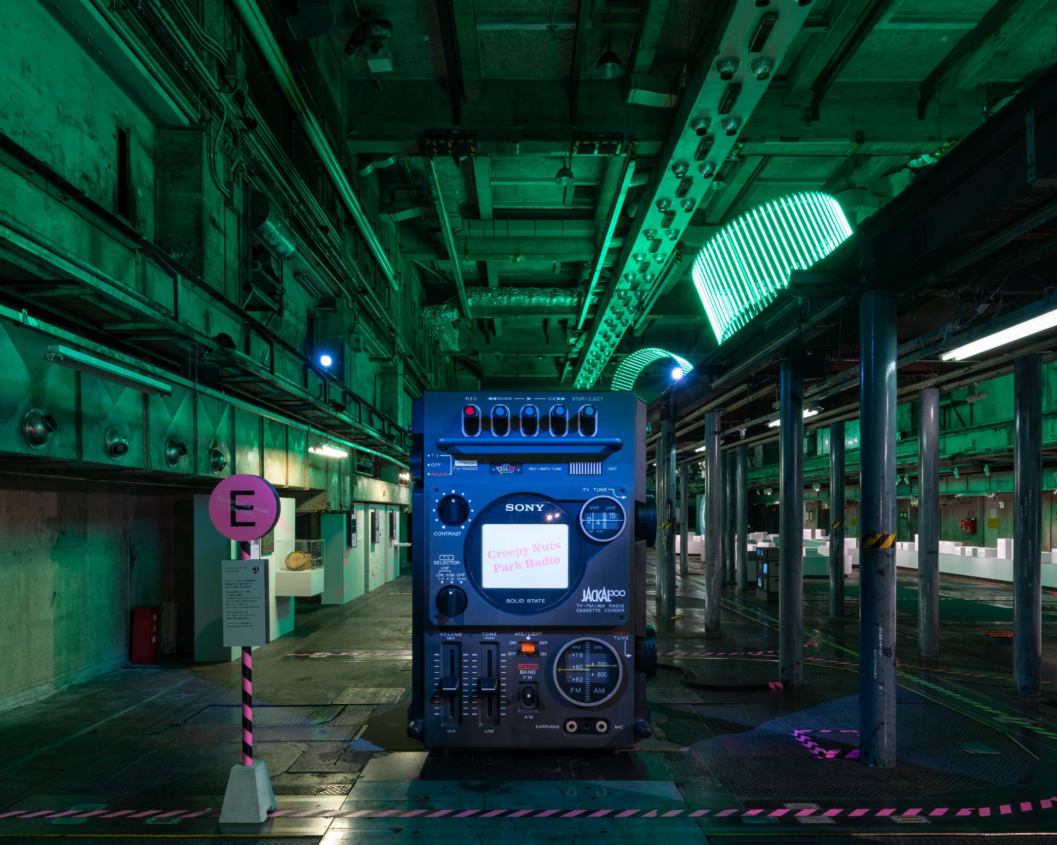 展示の様子。緑色の照明に彩られた空間にテレビ一体型ラジカセの巨大オブジェが展示されている。
