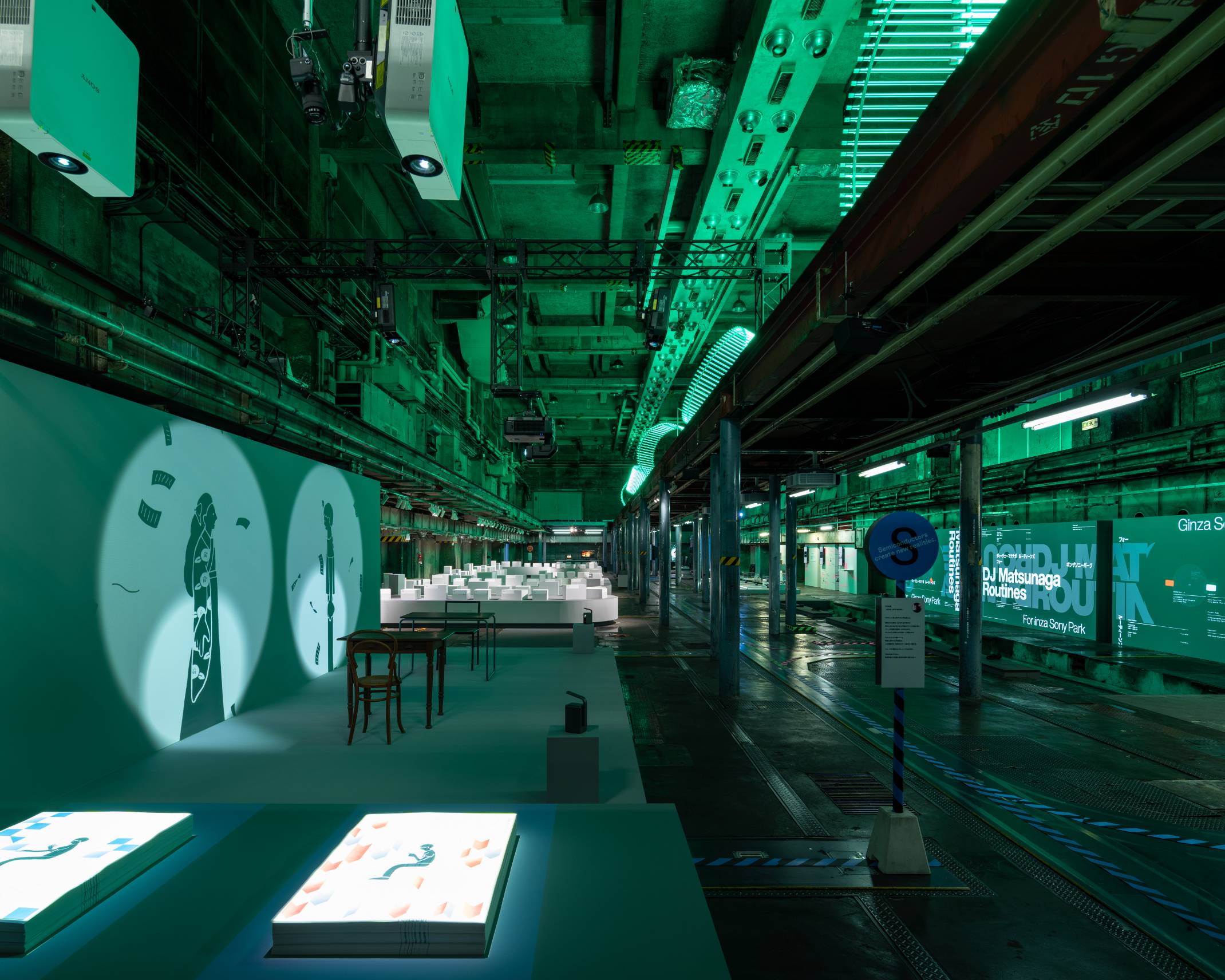 展示の様子。緑色の照明に彩られた空間の壁面に影絵のアニメーションが投影されている。