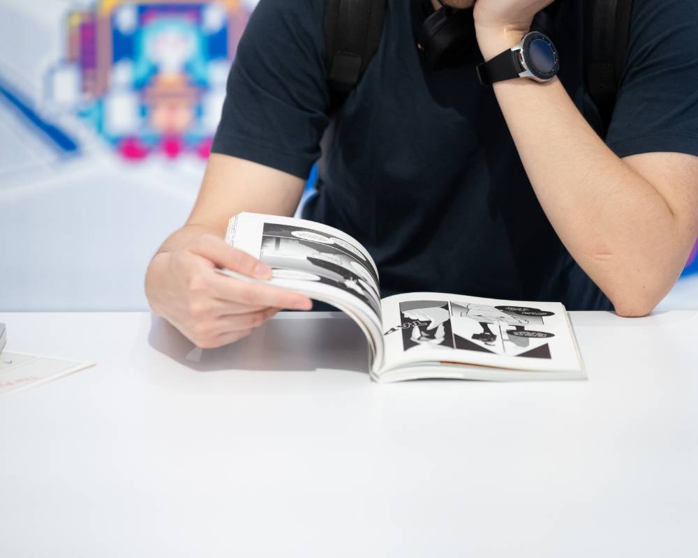 体験の様子。大きな壁面展示の前に設置されたテーブルで来場者がマンガの本を読んでいる。