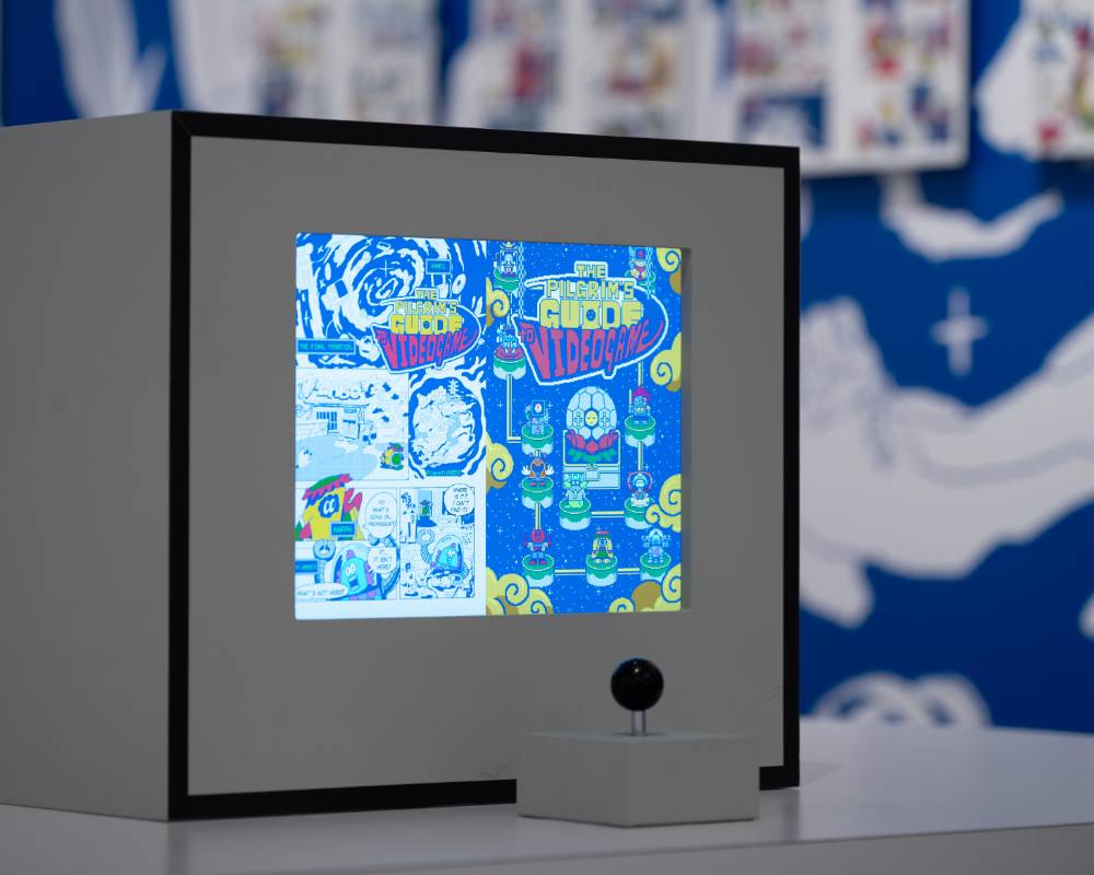 展示作品。モニターにマンガ『電遊道中膝栗毛』のページが映し出され、手前にはゲームのコントローラースティックが設置されている。