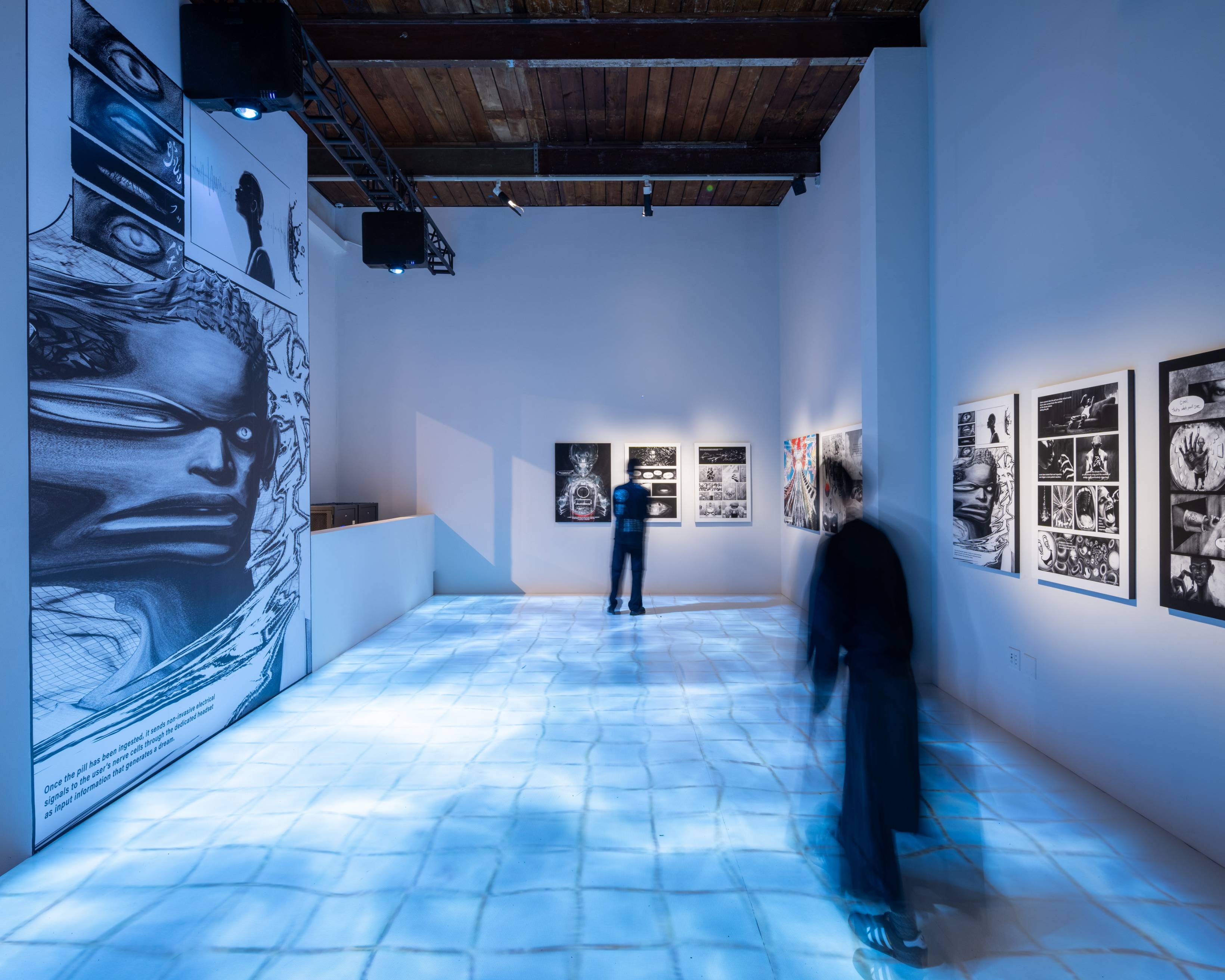 展示の様子。壁面にはマンガ『ドリームピル』のページが1枚ずつ展示され、床には水が張ったタイルのような映像が映し出されている。