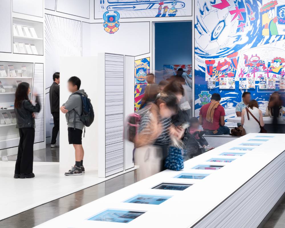 体験の様子。テーブルに埋め込まれたモニター上のマンガを読んだり、ベンチに着席して本でマンガを読んだり、さまざまな形でマンガを楽しんでいる。