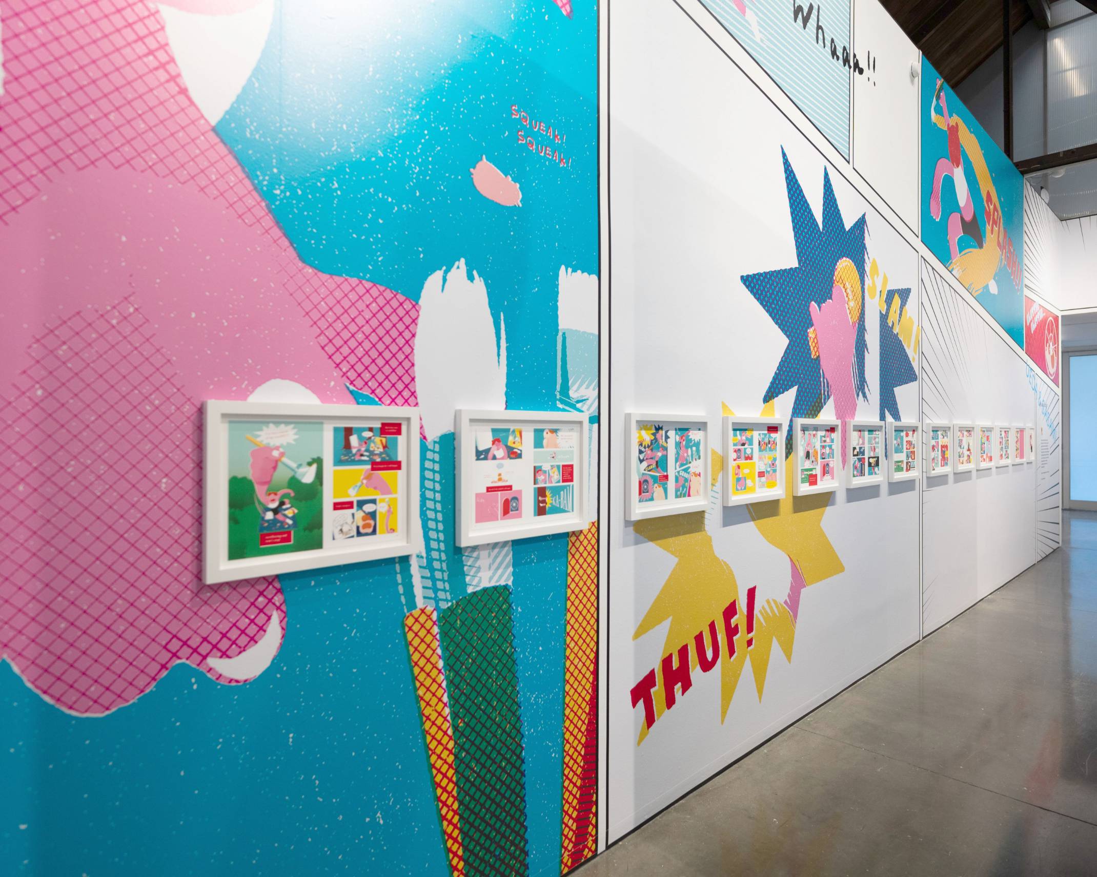 展示の様子。カラフルなグラフィックが大きく掲出された壁面に、マンガ『うえだとささみ』の見開きページが一つずつ白い木枠に入れて展示されている。