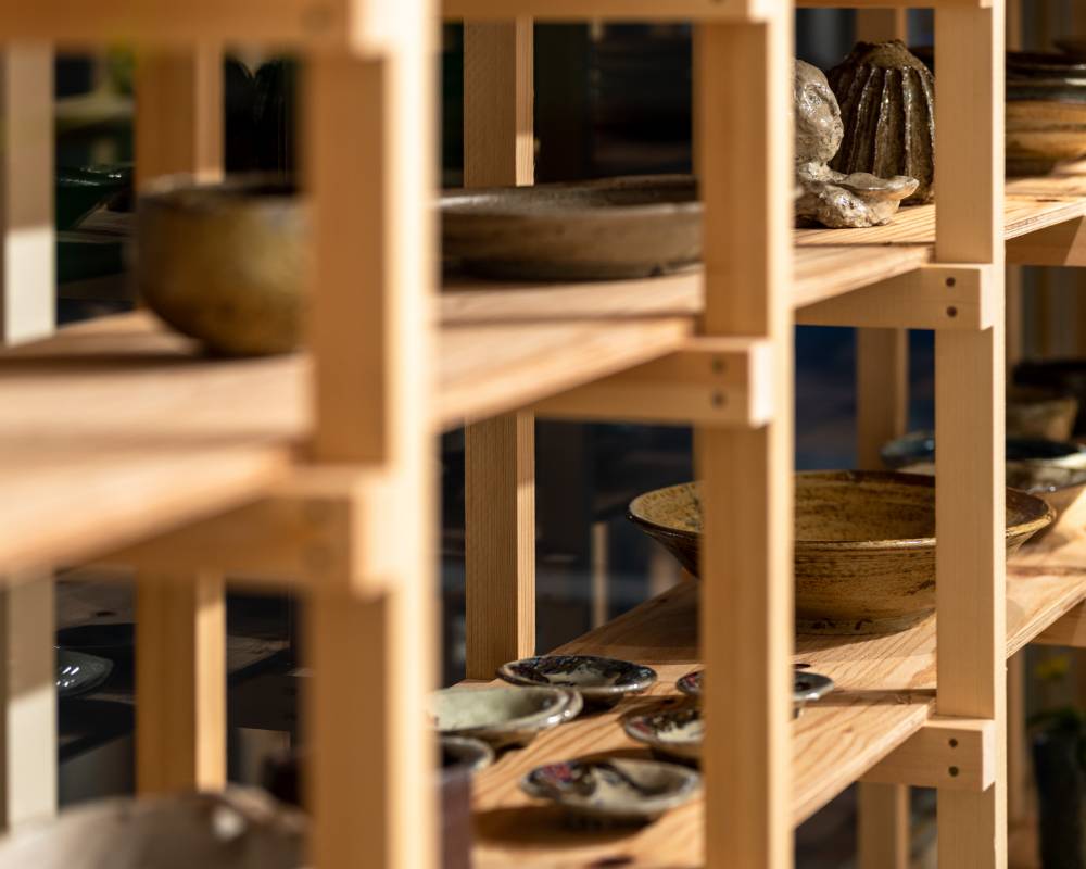 展示の様子。木製の棚に陶器のさまざまな食器や花器などが並んでいる。