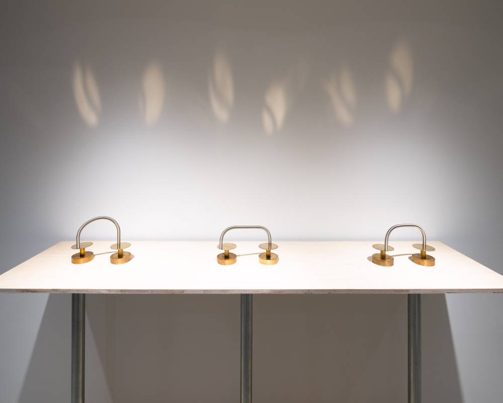 展示の様子。金属のバネと円で構成された作品が３つ並び、バネの動きによって壁に光が映し出されている。