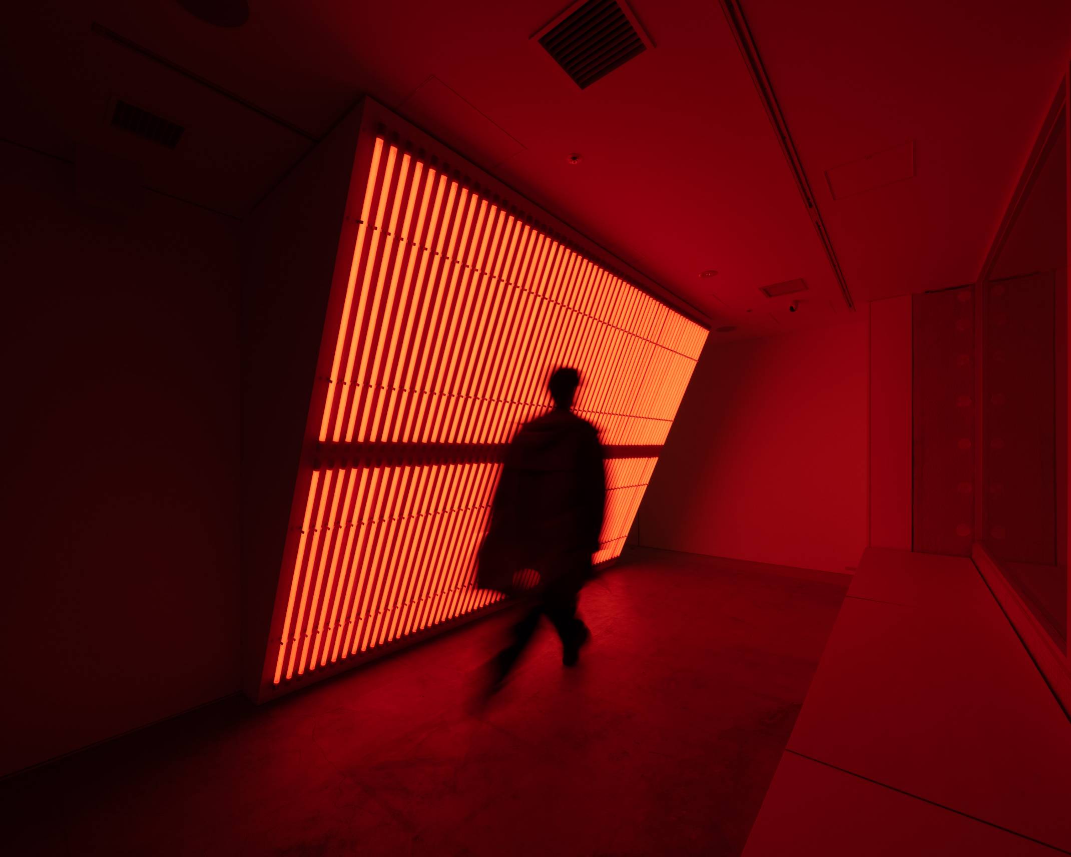 内観。オレンジ色の光のインスタレーションの前を歩くひとがいる。