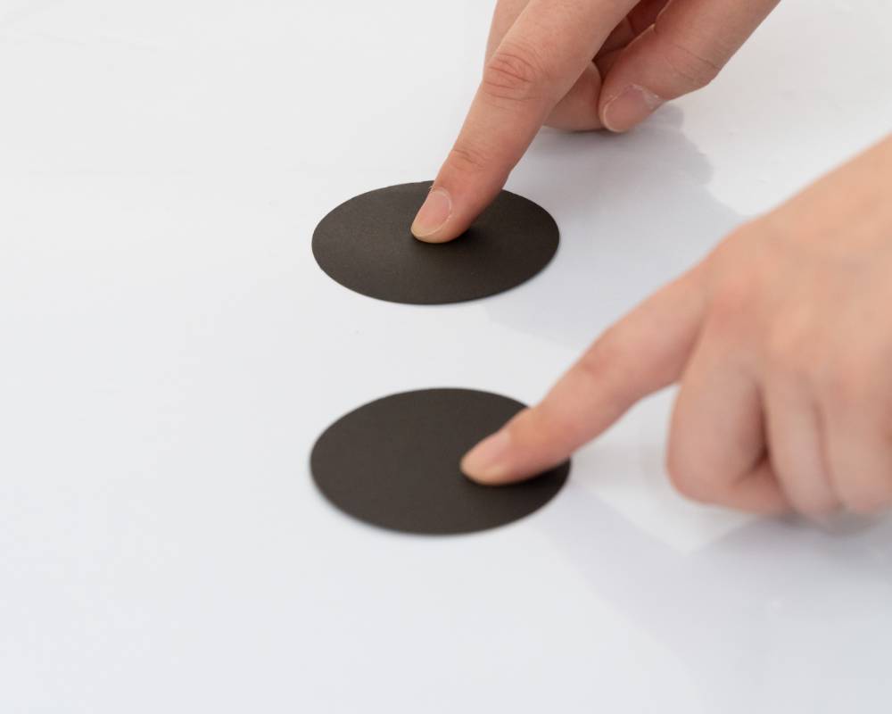 体験の様子。２つの黒い円形のシートの上に、両手の人差し指を乗せている。