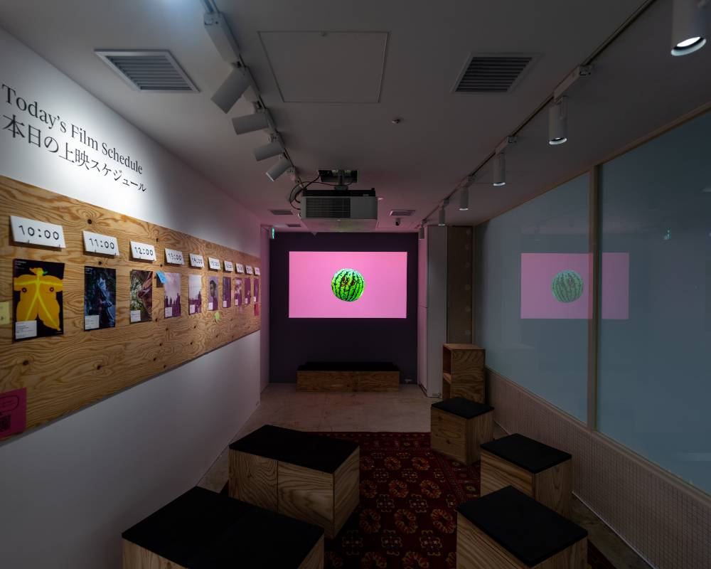 内観。展示スペース奥の壁面には映像が投影され、その手前にはいくつかのスツールが置かれている。