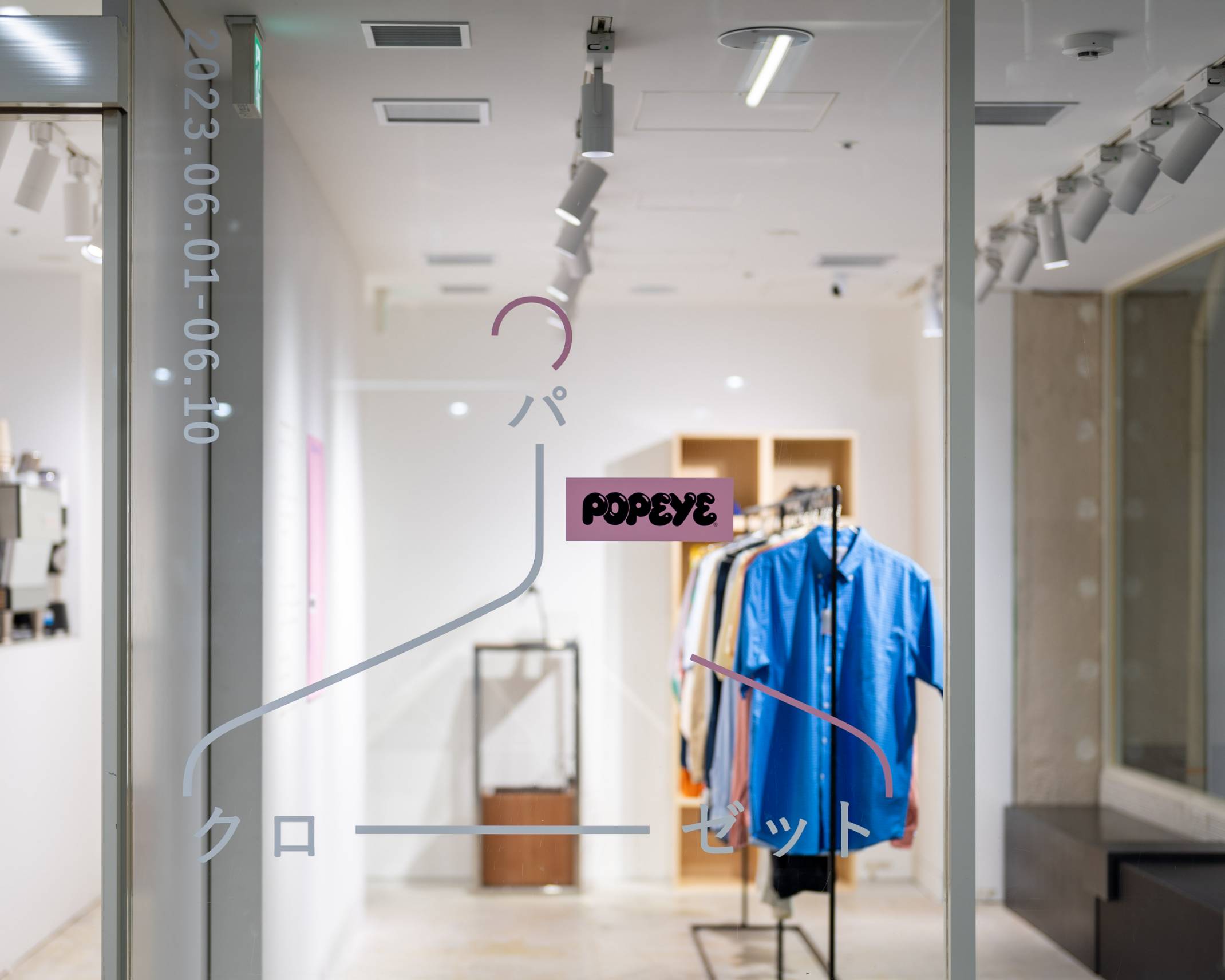 外観。ガラス面にはPOPEYEのロゴがあしらわれたハンガーのようなグラフィックが掲出され、展示スペース中央にはさまざまな洋服が吊り下げられたハンガーラックが置かれている。
