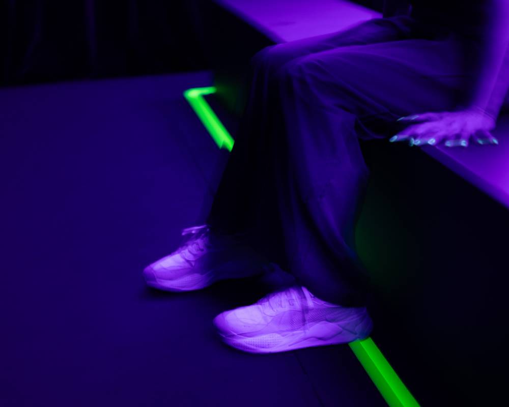 体験の様子。紫がかったうす暗い空間の中でベンチに着席して体験する来場者の足元が振動している。