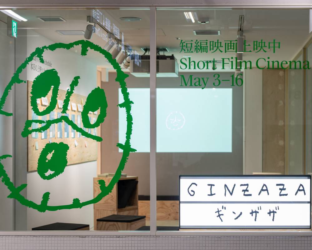 外観。展示スペースにはいくつかのスツールが置かれ、壁面にプロジェクタの光が投影されている。