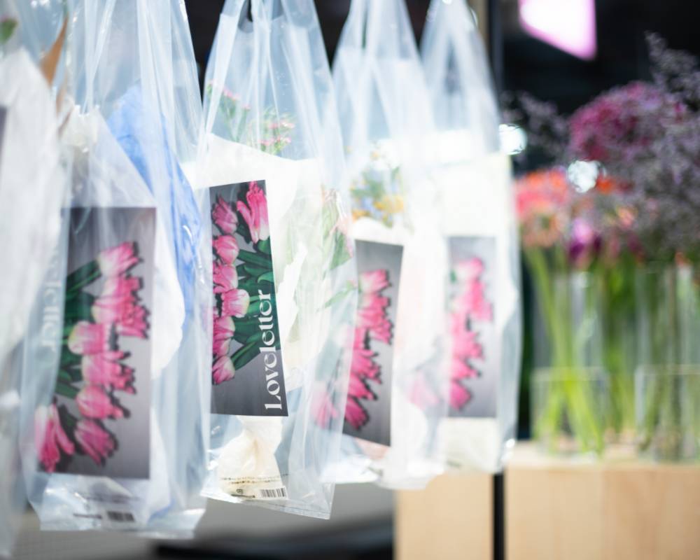展示の様子。お花とキービジュアルのカードが入った透明ビニールのショッパーが複数吊り下げられている。