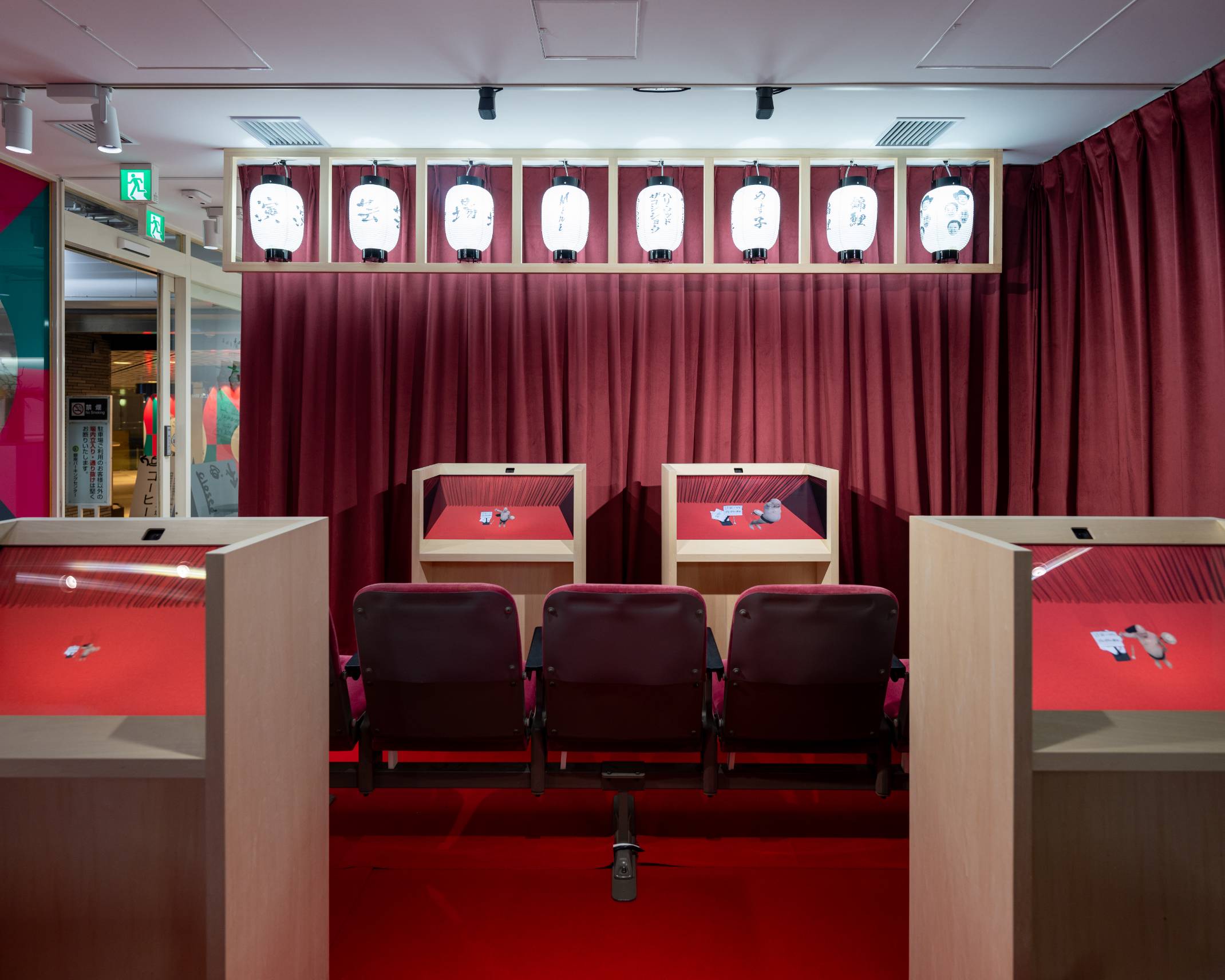 内観。えんじ色のカーテンや提灯が飾られた空間の中に木製の台に覆われたモニターが並んでいる。