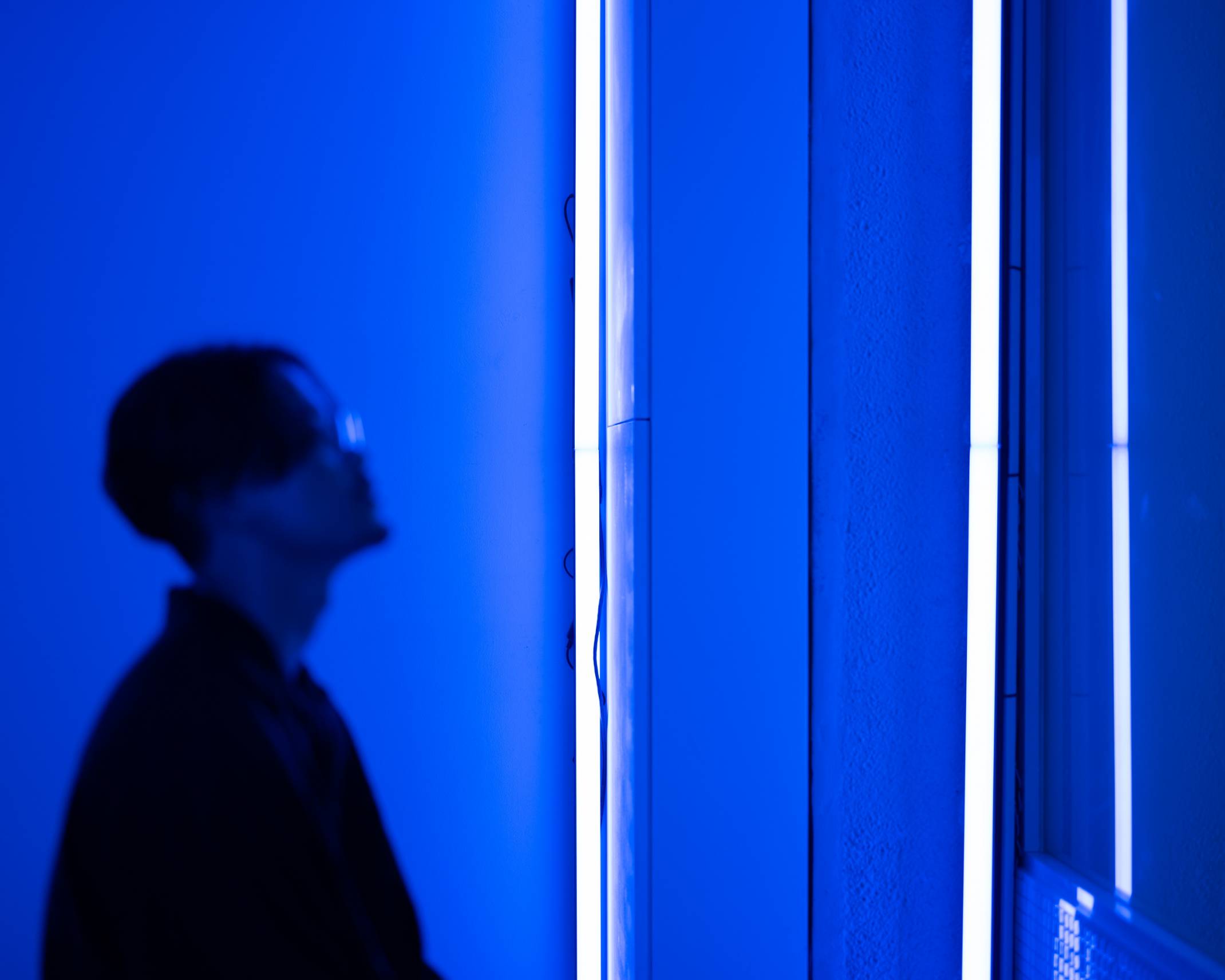 体験の様子。縦に置かれた2本のライン照明によって空間全体が青くなったスペースで、来場者は少し上を見上げている。