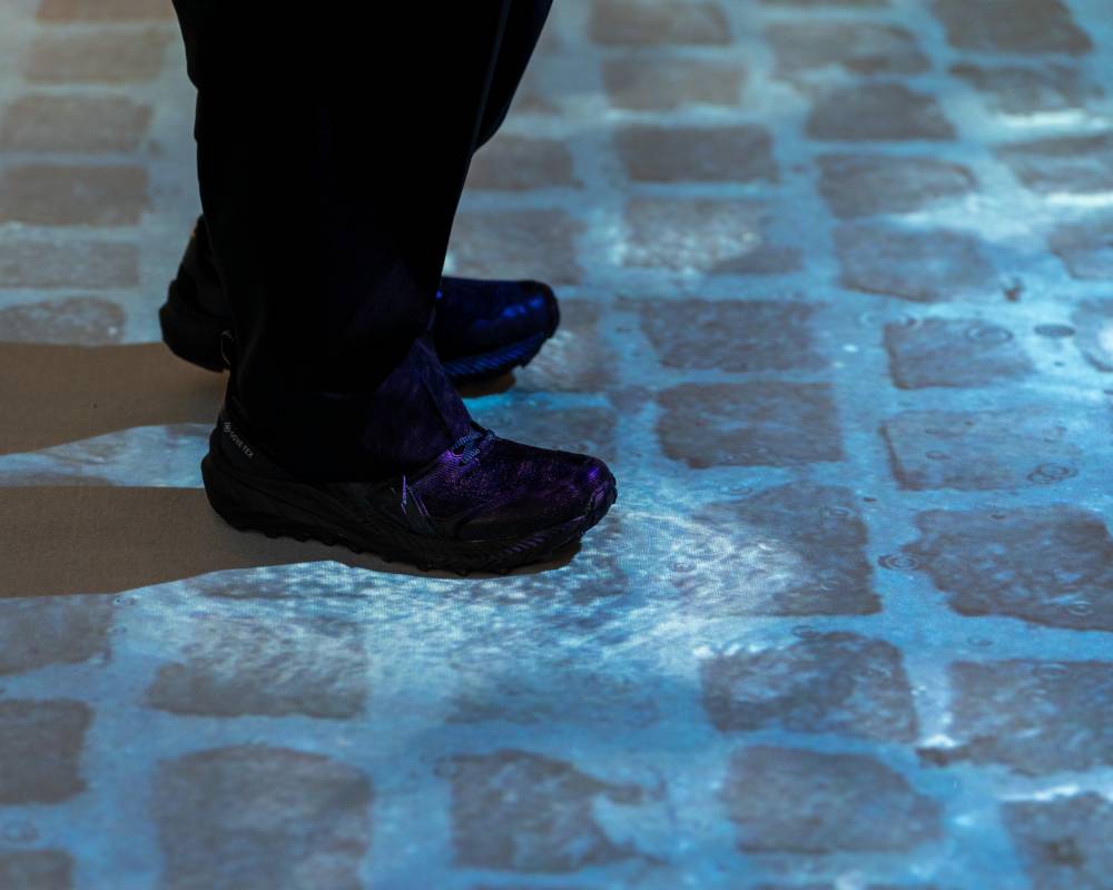 体験の様子。床面に映し出されたレンガの敷石に溜まった水の上を歩いている。