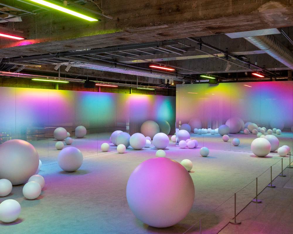 展示の様子。カラフルに色づく光に満たされた空間に大小さまざまな球体が点在している。