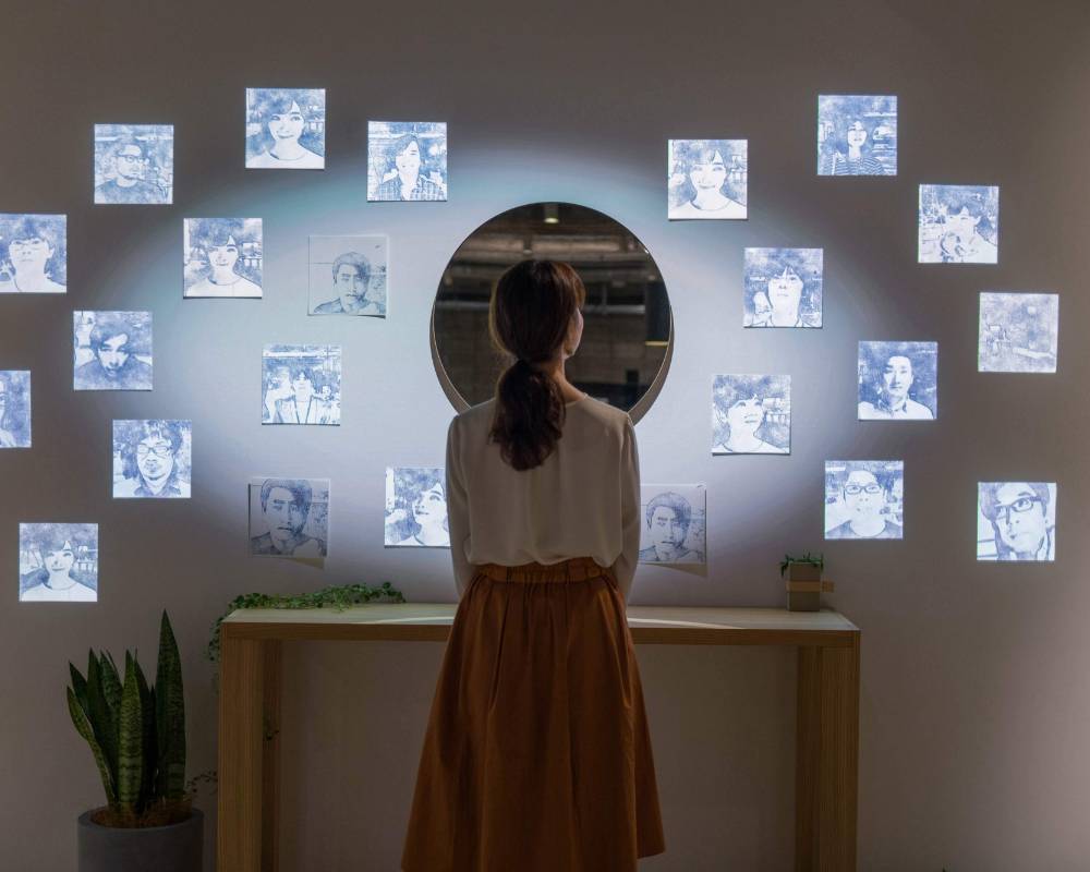 体験の様子。複数の顔が映し出されている壁の中央にある丸い鏡の前に来場者が佇んでいる。